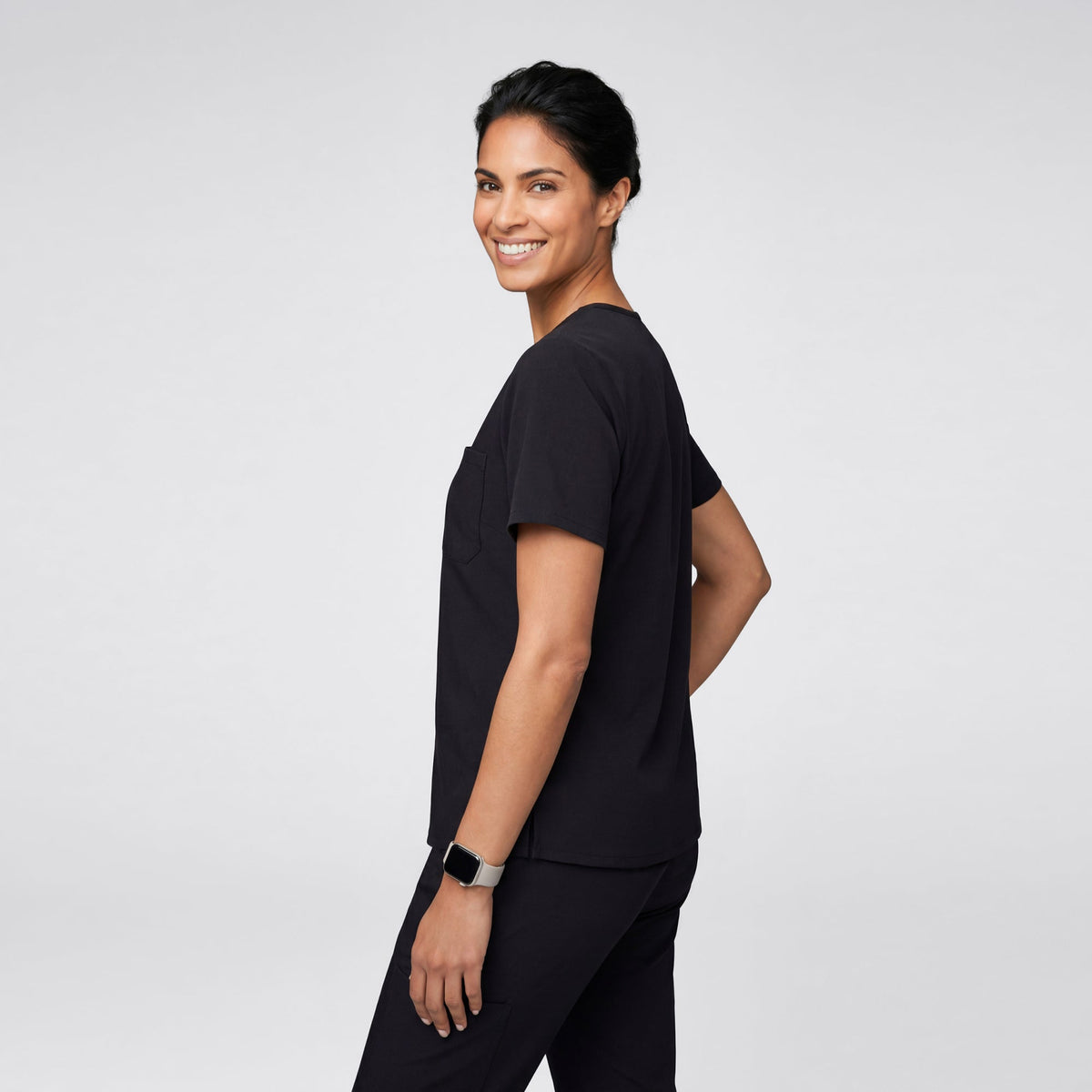 A person shown from the back wearing an Eco Black scrub top with short sleeves, displaying the clean and minimal back design.