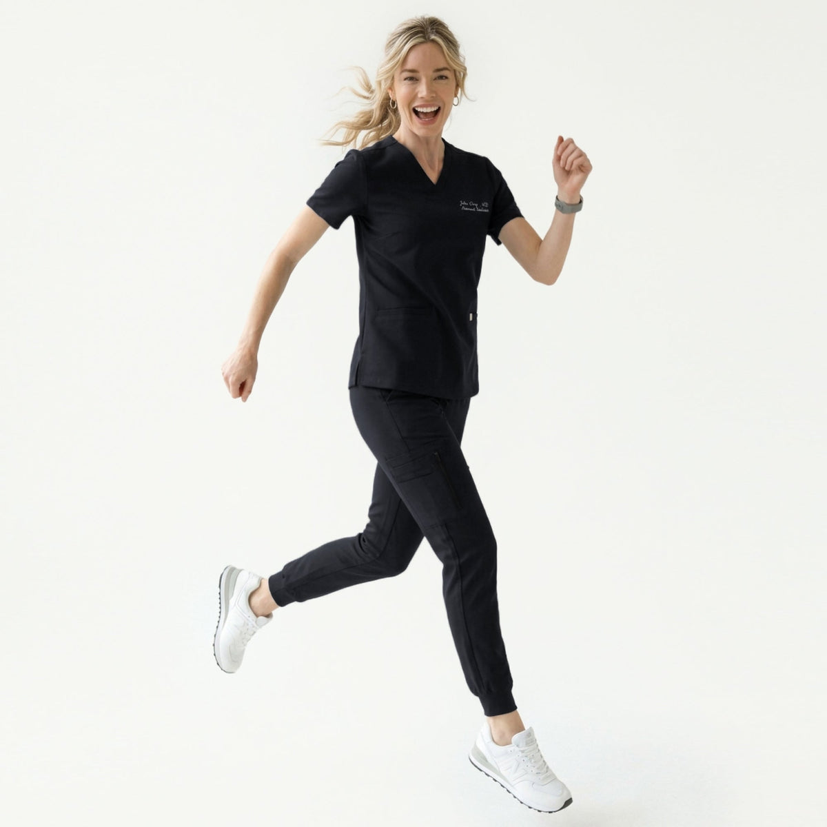 Woman wearing a black V-neck scrub top with embroidered name and double front pockets, paired with matching black scrub pants,Eco Black