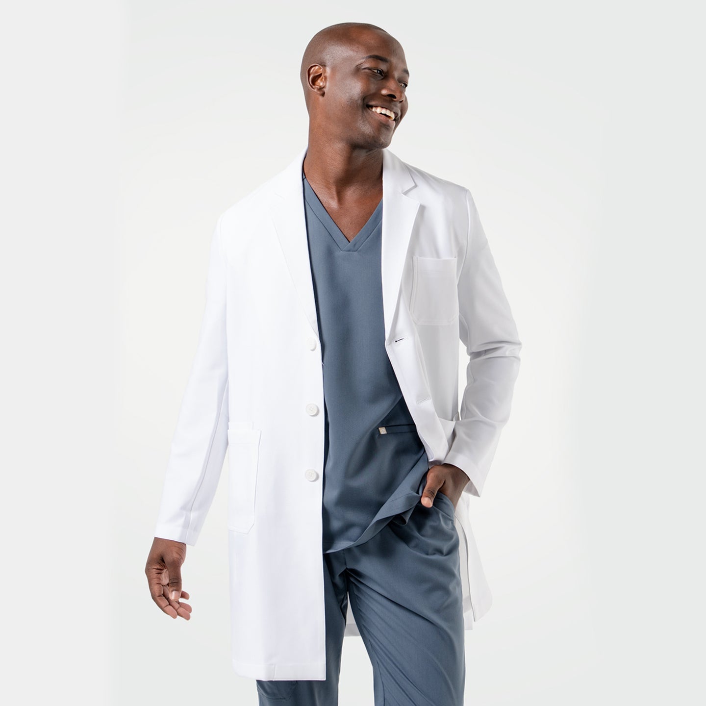 Laughing in the Men's LCM-101 Lab Coat in White over medical scrubs, one hand in the pocket, full body view