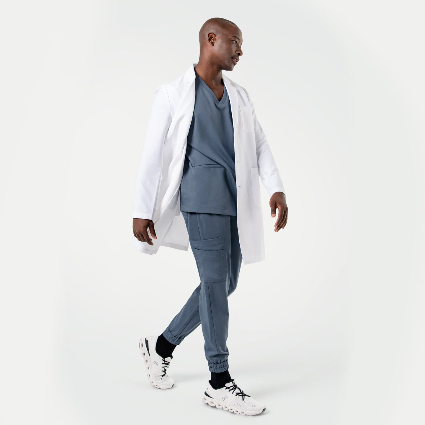 Walking in the Men's LCM-101 Lab Coat in White over medical scrubs, side view, full body shot