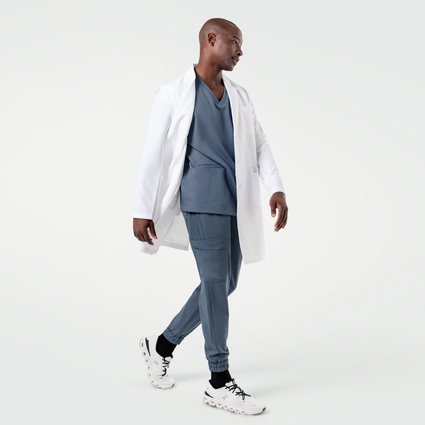 Walking in the Men's LCM-101 Lab Coat in White over medical scrubs, side view, full body shot