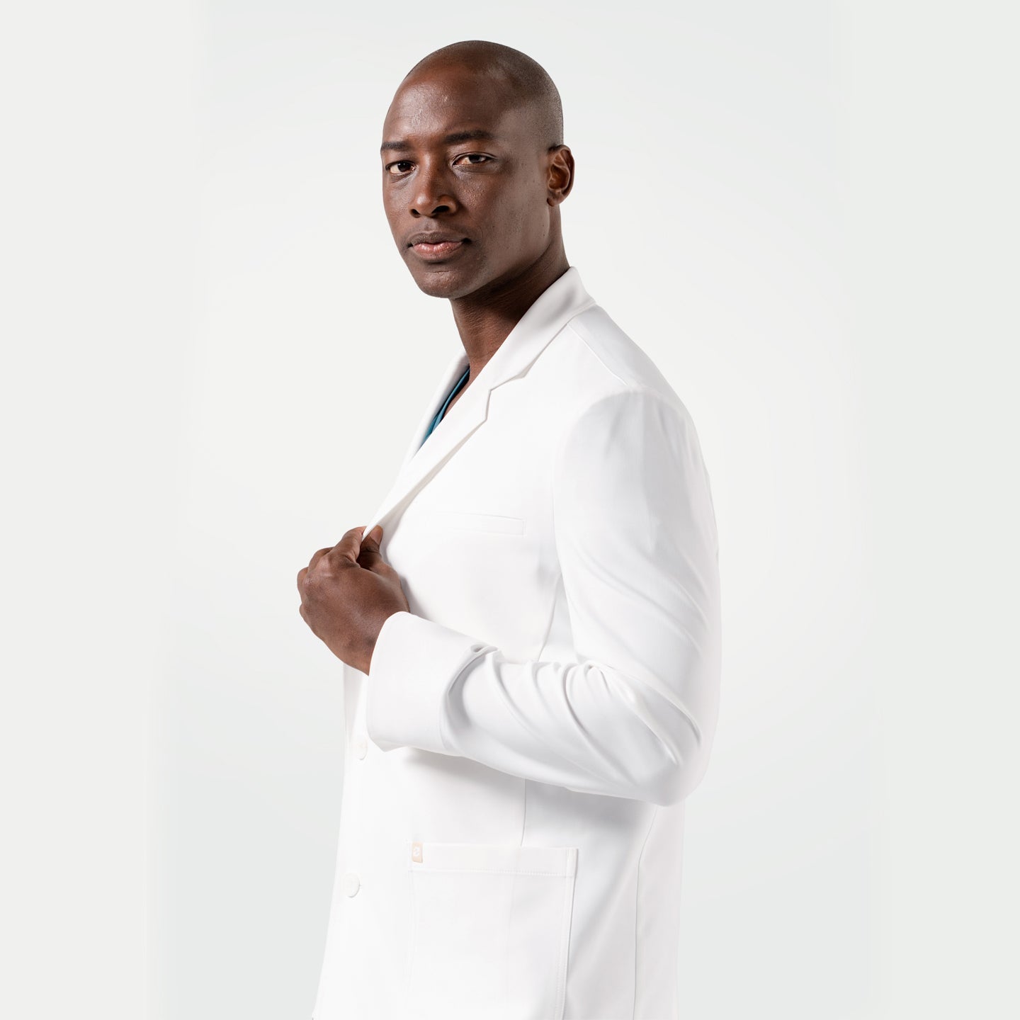 Posing in the Men's LCM-102 Lab Coat in White over medical scrubs, holding the lapel with one hand and looking at the camera, upper body view