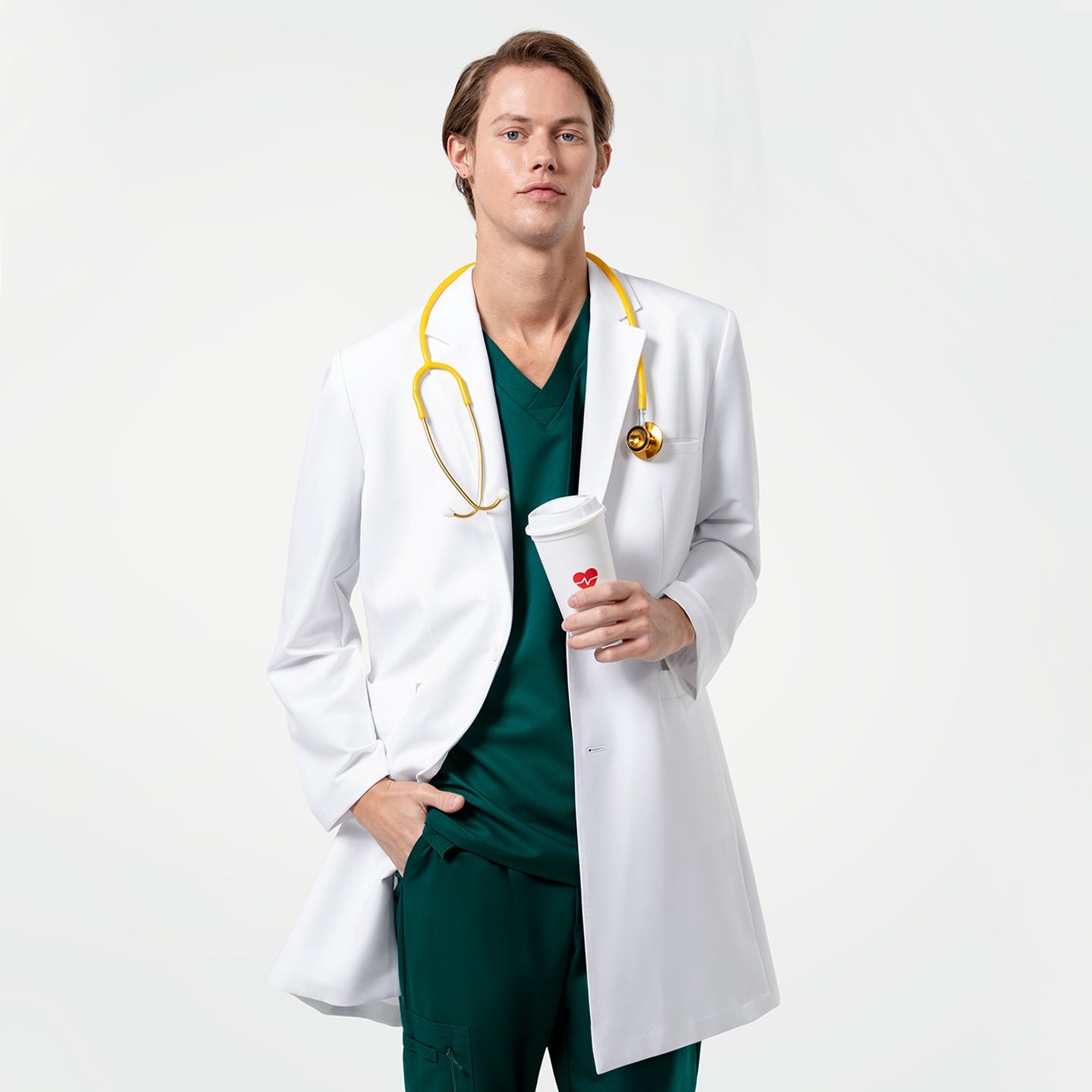 Holding a coffee cup, wearing the Men's LCM-103 Lab Coat in White over medical scrubs with a yellow stethoscope around the neck, one hand in the pocket