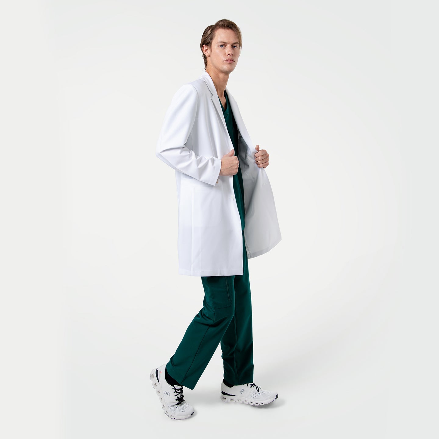 Person wearing a white lab coat over pine green scrubs on a white background