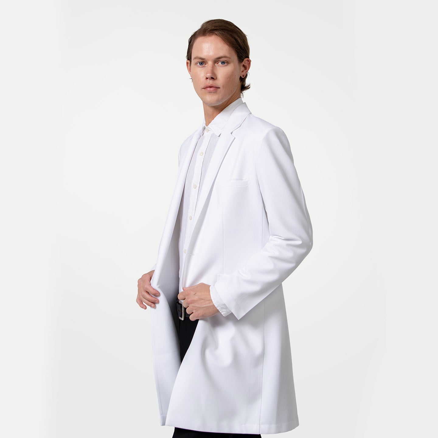 With a composed expression, a male healthcare professional wears a white coat over a white dress shirt and black trousers