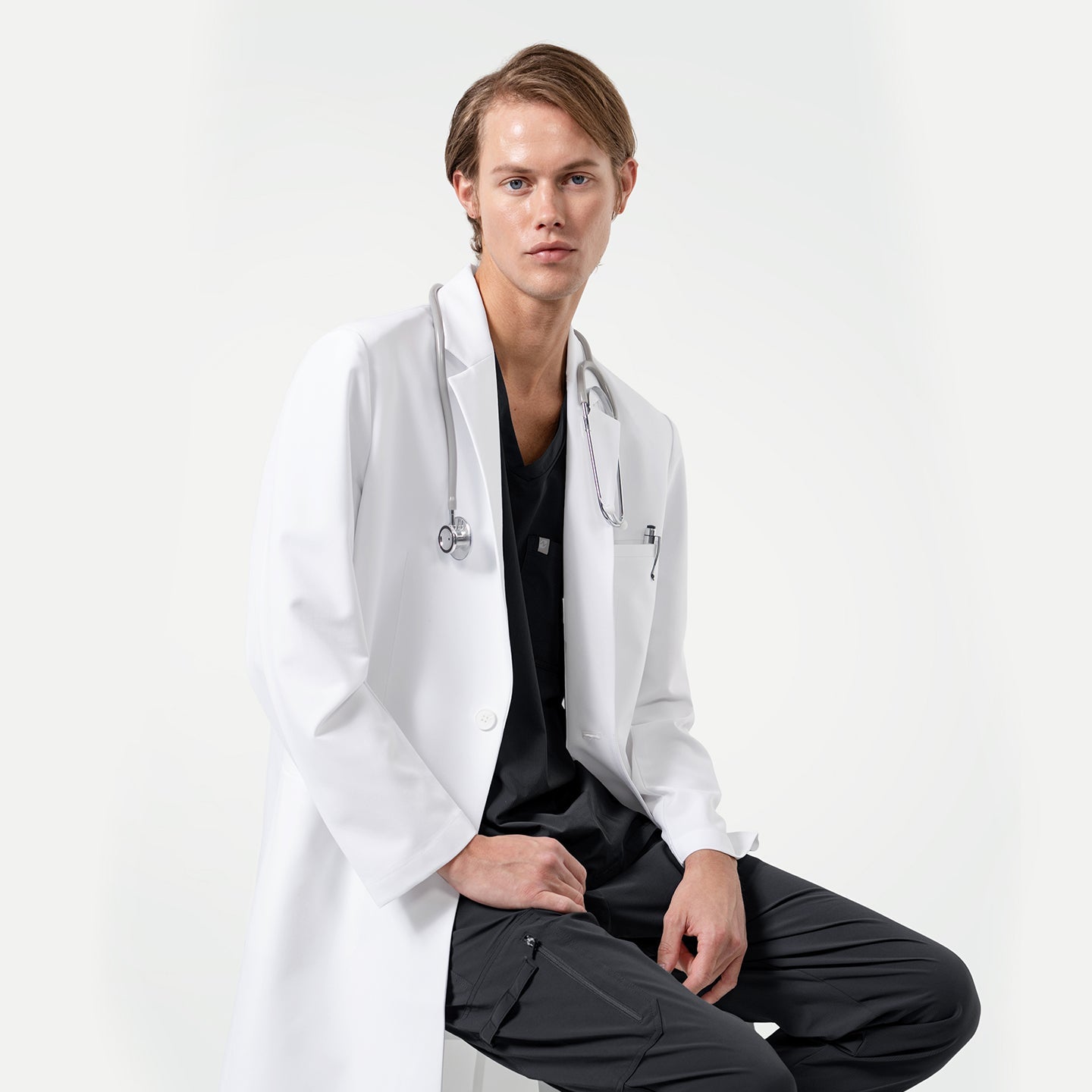 Lcm-103 men’s white lab coat with stethoscope, styled over black scrubs, modern tailored design for doctors and healthcare professionals.
