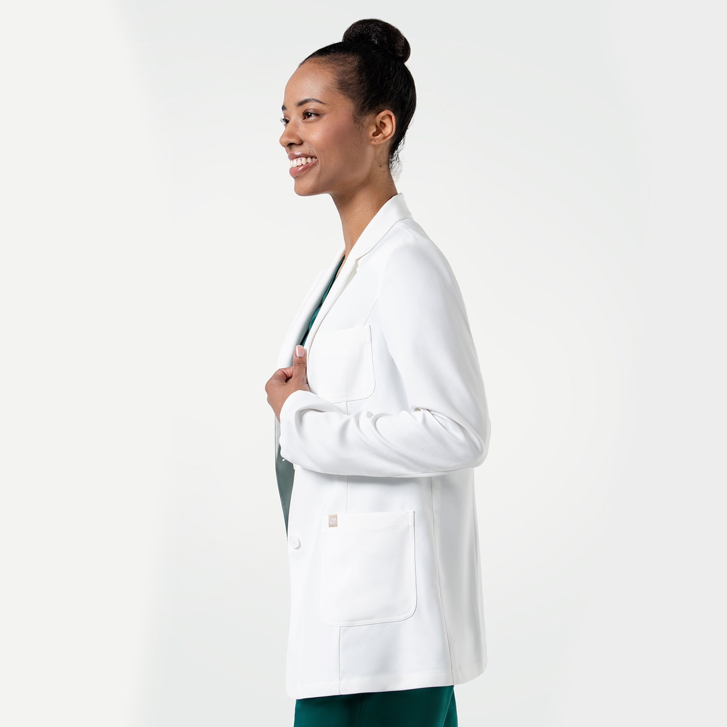 Upper body shot of the model wearing the Women's LCW-101 Lab Coat over pine green scrubs, smiling while looking to the side