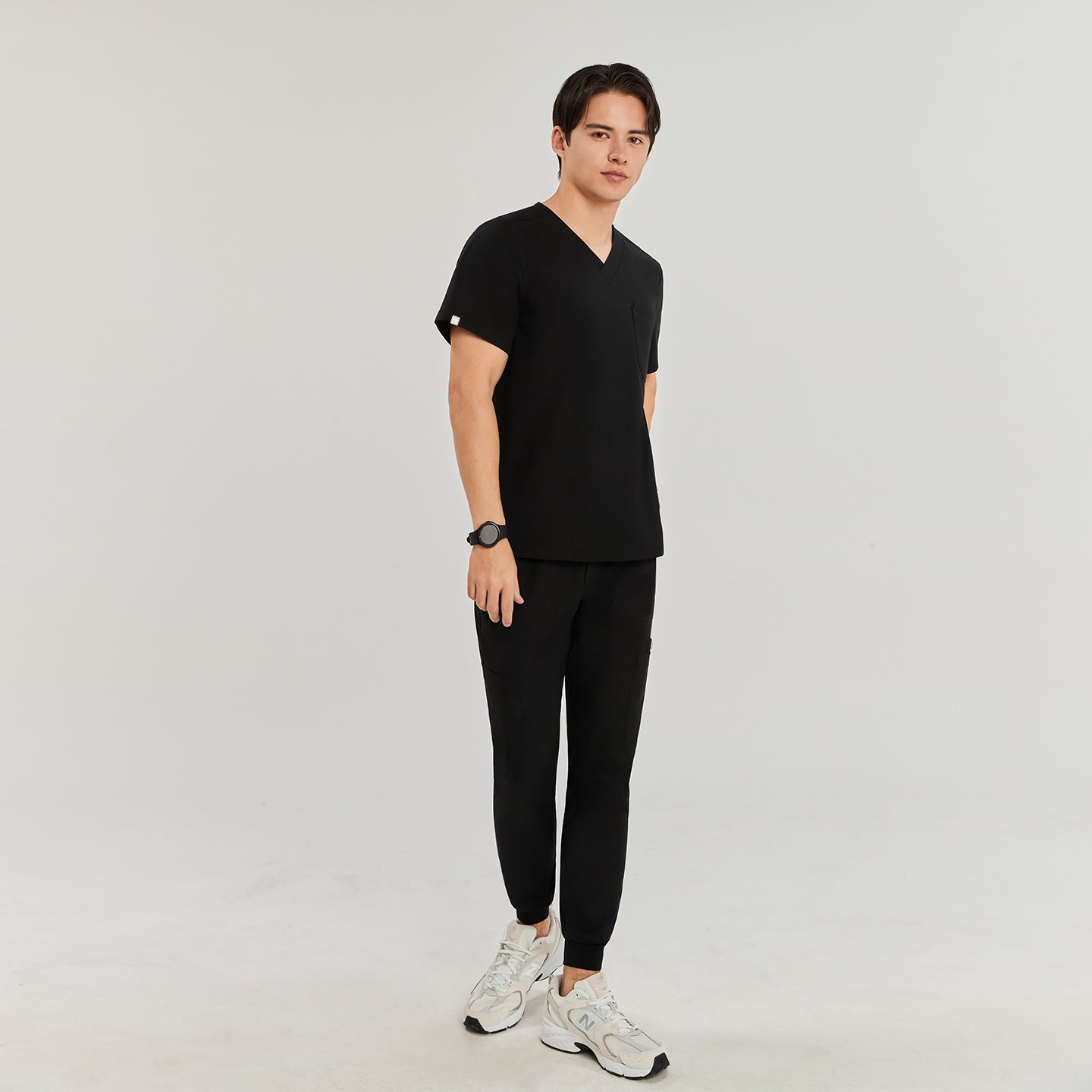 Man in black Zenir scrub top with chest pocket, standing and looking at the camera, full-body view,Eco Black