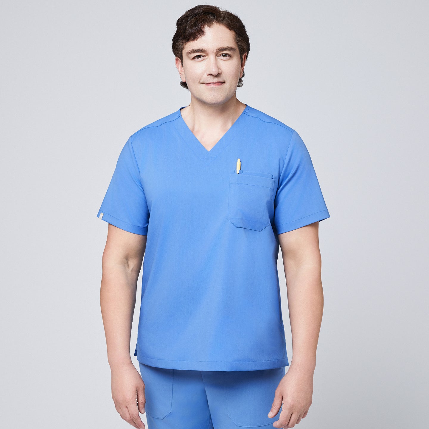 Male model wearing a ceil blue V-neck scrub top with a chest pocket holding a pen, paired with matching scrub pants, designed for a professional medical setting,Ceil Blue
