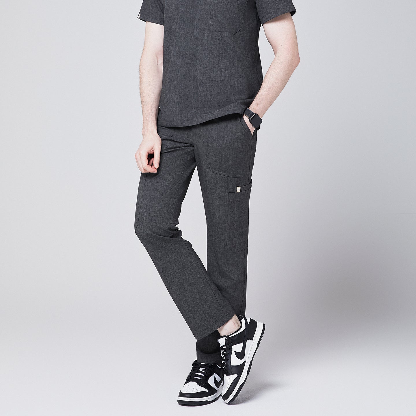man standing cross-legged, showcasing Zenir charcoal-gray zipper straight scrub pants with black-and-white sneakers and a smartwatch,Charcoal Gray