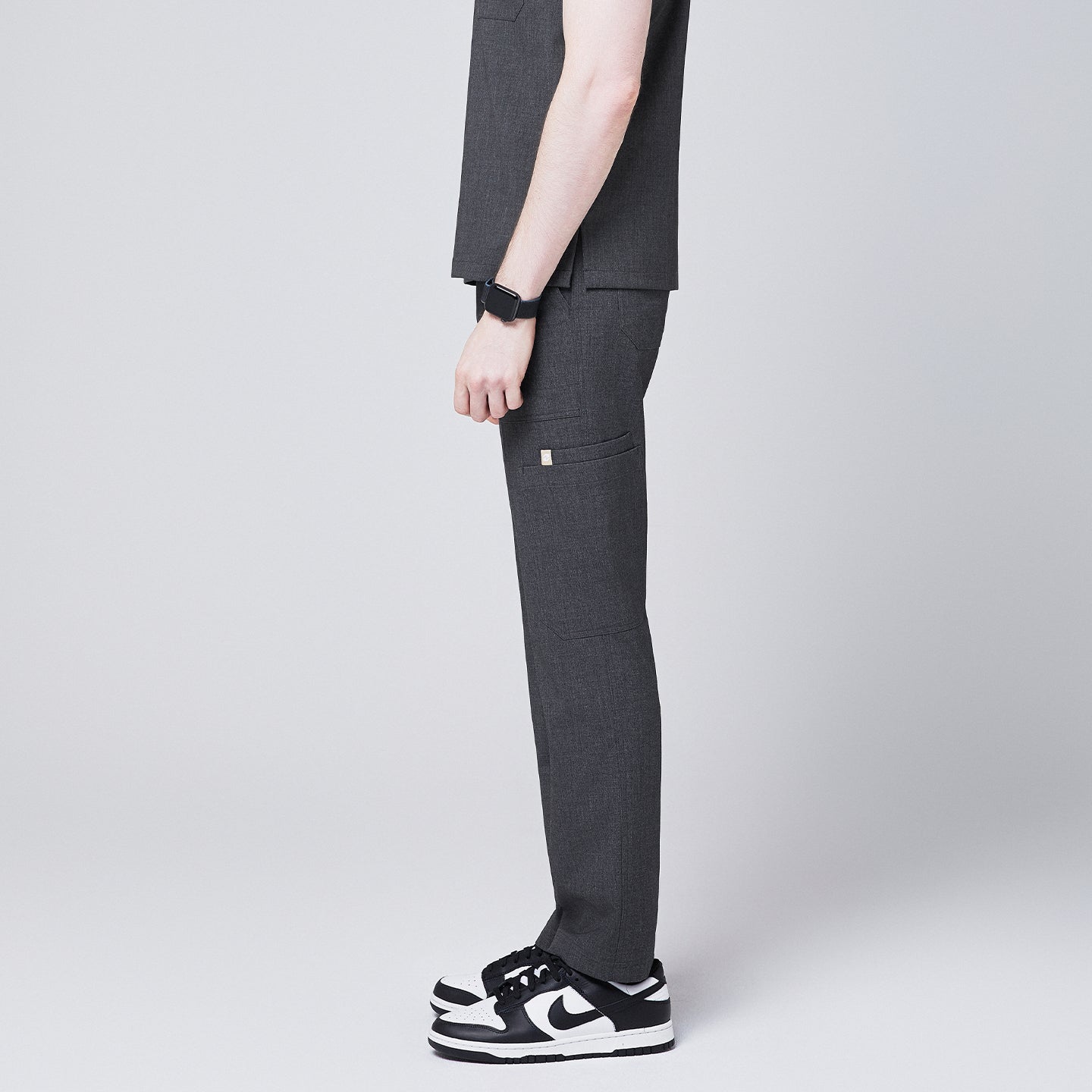 man showcasing the side view of Zenir charcoal-gray zipper straight scrub pants, paired with black-and-white sneakers and a smartwatch,Charcoal Gray
