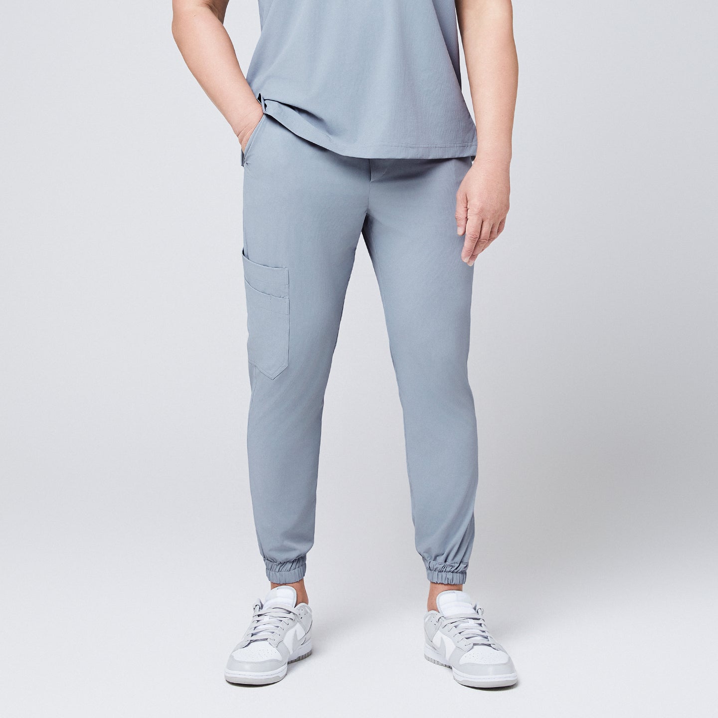 Front view of cool gray jogger scrub pants with a cargo pocket and elastic cuffs, paired with gray Nike sneakers,Cool Gray