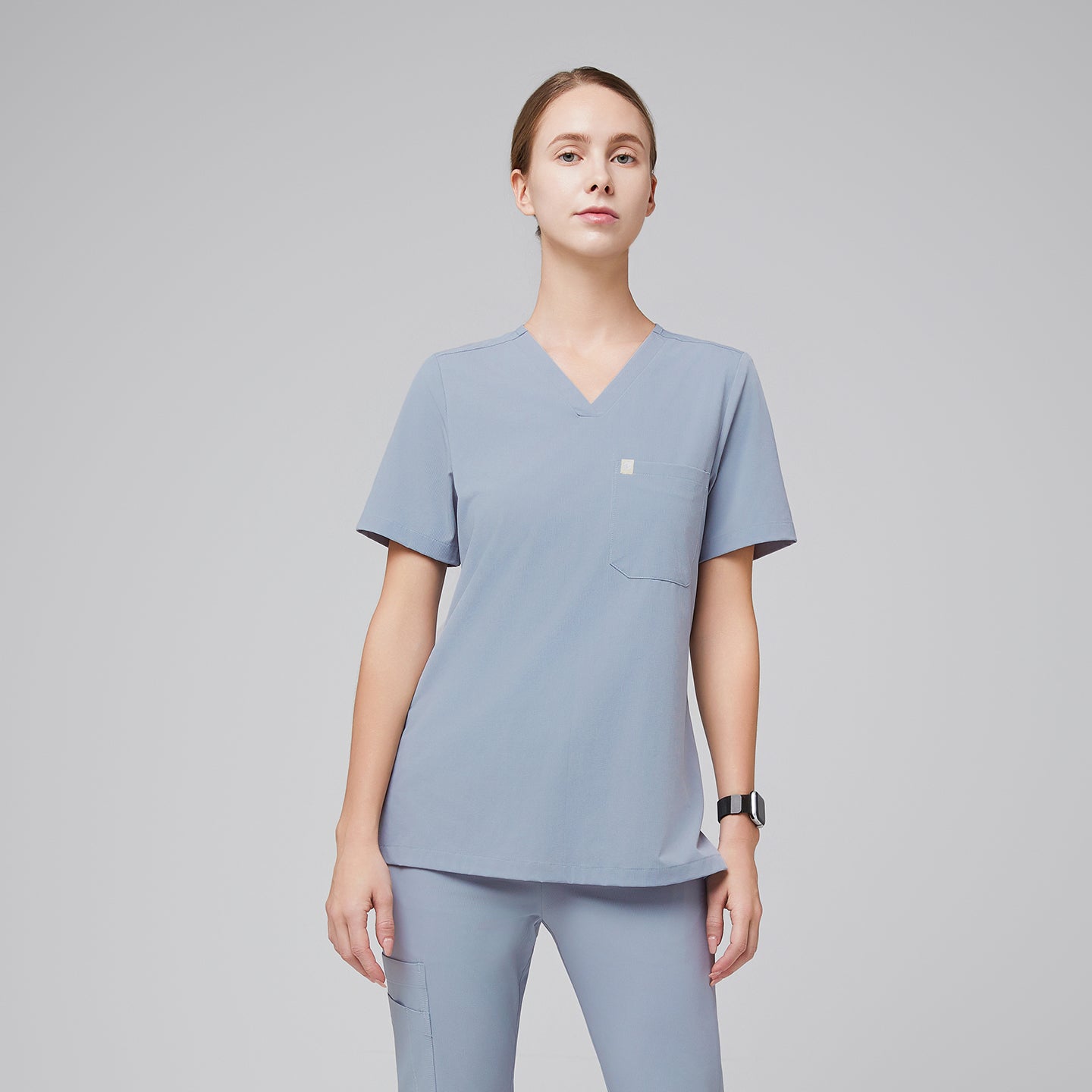 Female healthcare professional wearing a cool gray V-neck scrub top and pants, standing with a confident posture,Cool Gray