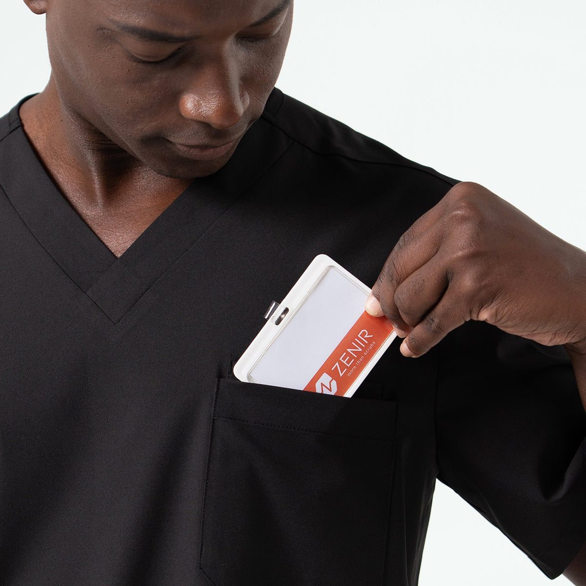 Close-up of a medical professional placing a ID badge into the chest pocket of an Eco Black scrub top, highlighting the secure pocket design and smooth fabric texture.
