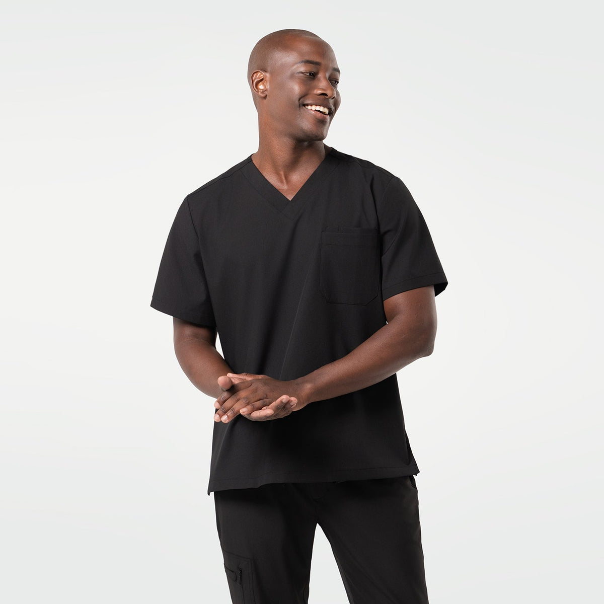 A smiling male model wearing a short-sleeve 3 Pocket scrub top in Eco Black.
