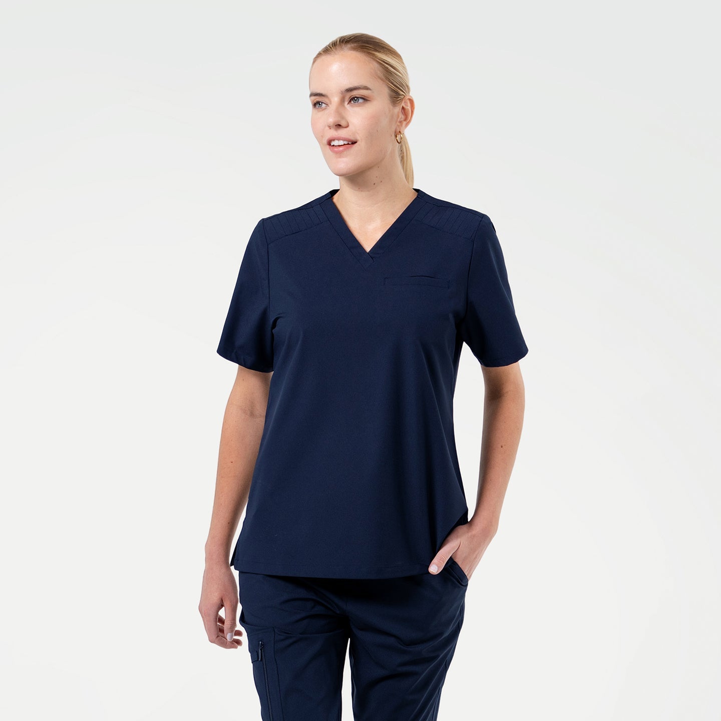 A Female model wearing Eco Navy ZenFlex scrub top with matching scrub pants.