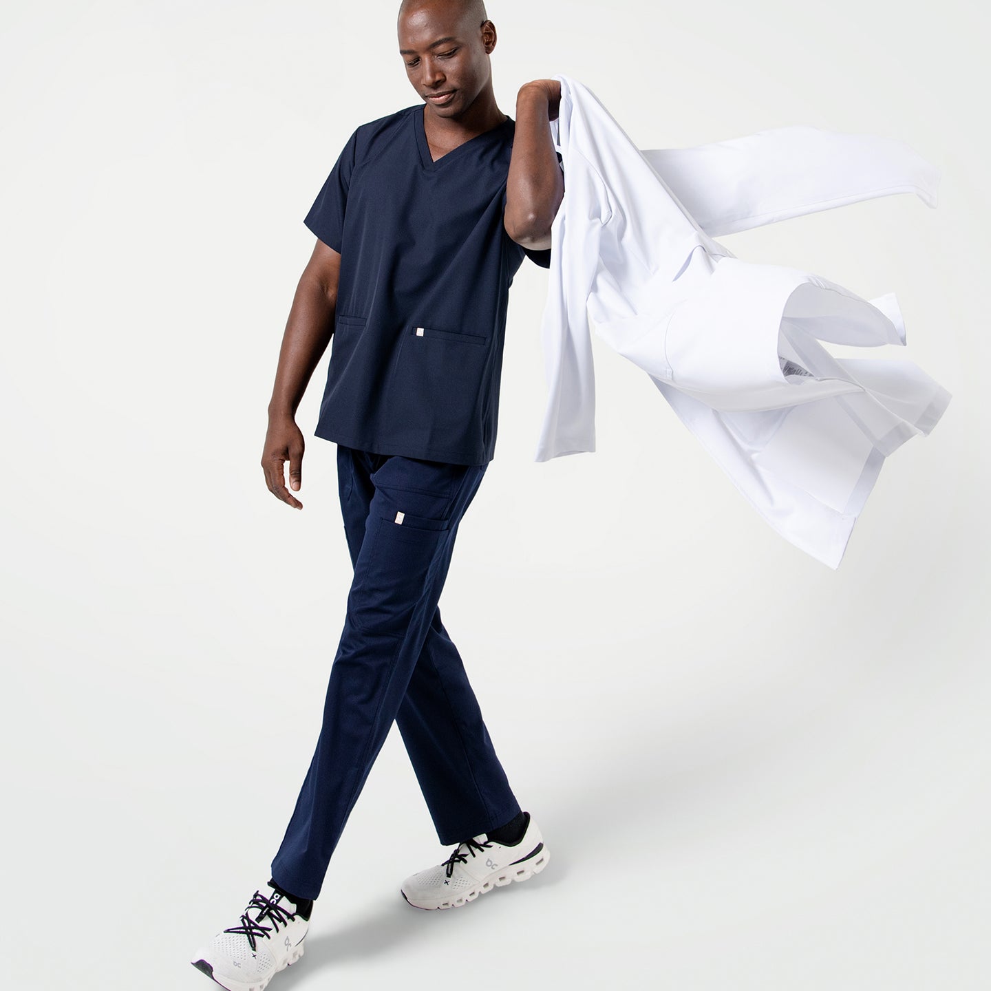 Male model in Eco Navy scrubs walking with a relaxed stride, holding a LCM-02 casually over his shoulder.