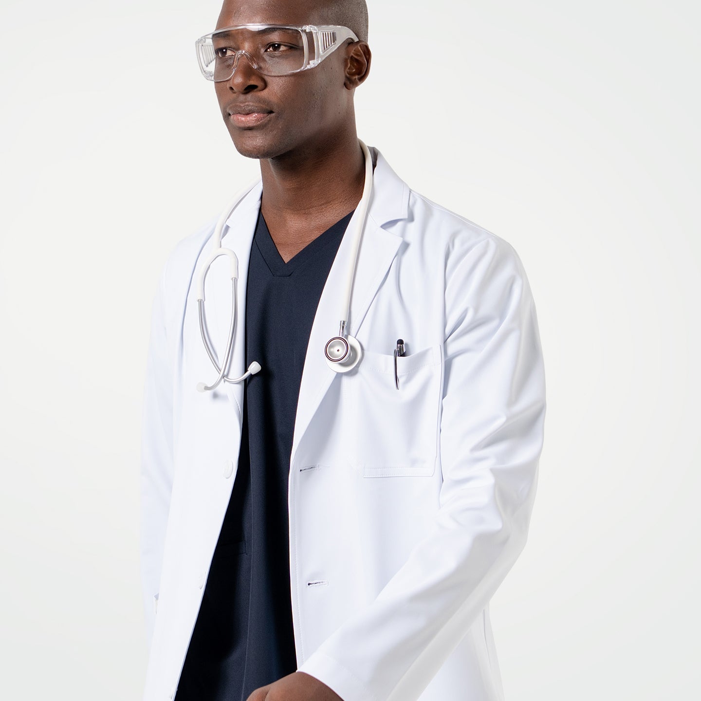 Male model wearing the LCM-02 White Lab Coat over Eco Navy scrubs, accessorized with clear protective glasses and a stethoscope draped around the neck.