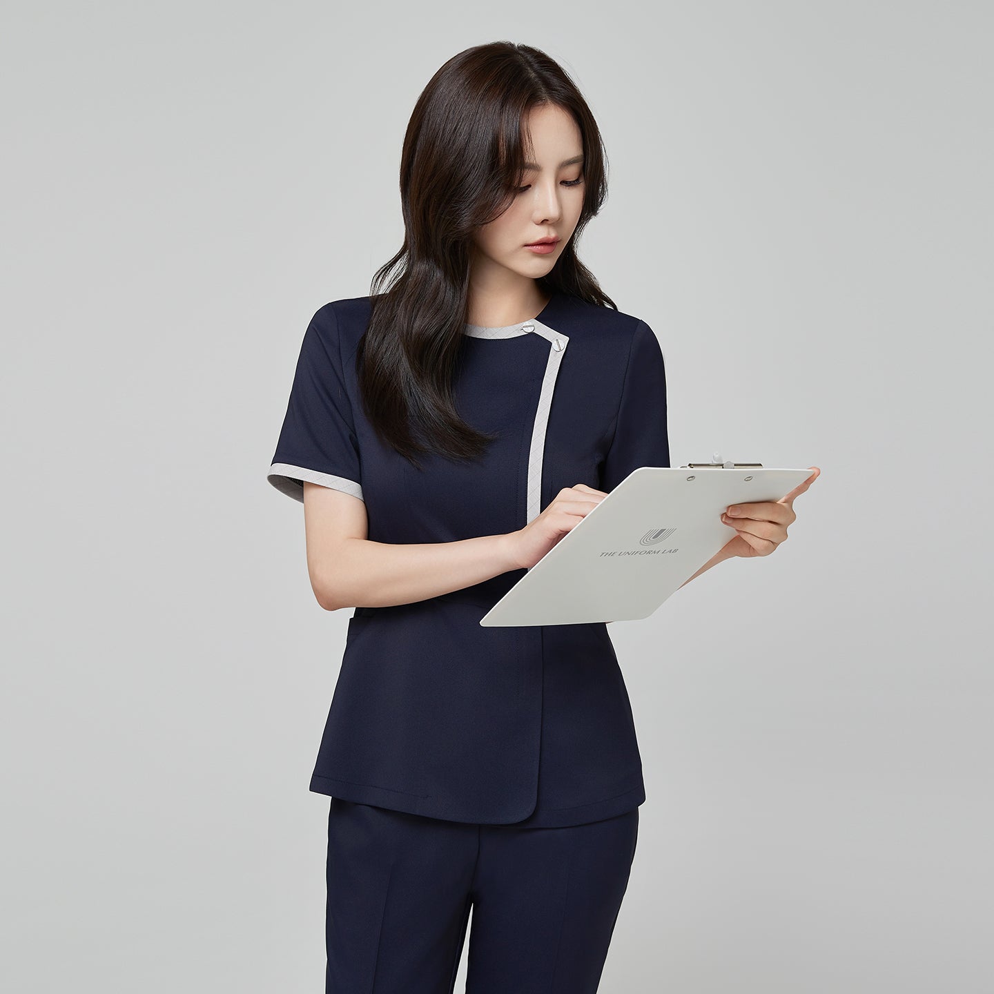 Side angle of TUL NS-174 Women’s Check Gray Round Collar Scrub Top in Mir Navy, emphasizing the contrasting gray piping on the sleeves and neckline.