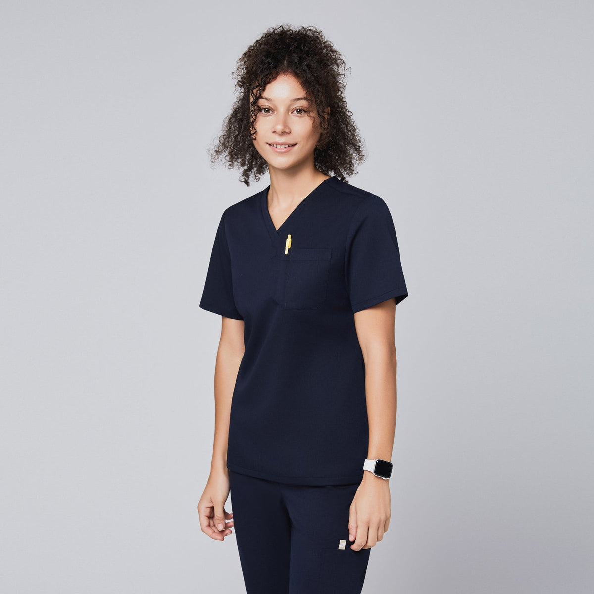 Woman in a navy scrub top with a chest pocket holding a yellow pen, smiling,Navy