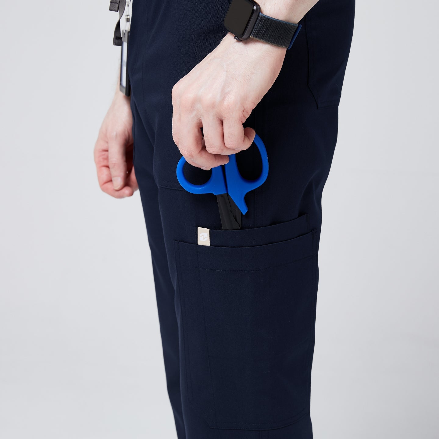 Close-up of navy jogger scrub pants with a side pocket holding blue medical scissors, showcasing functionality and utility.Navy