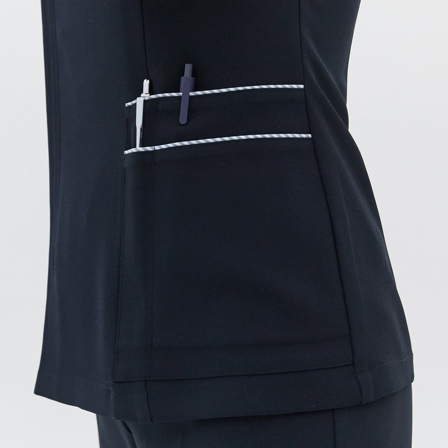 A detailed view of the side pocket on a navy round-neck top, featuring white trim and holding two pens,Navy