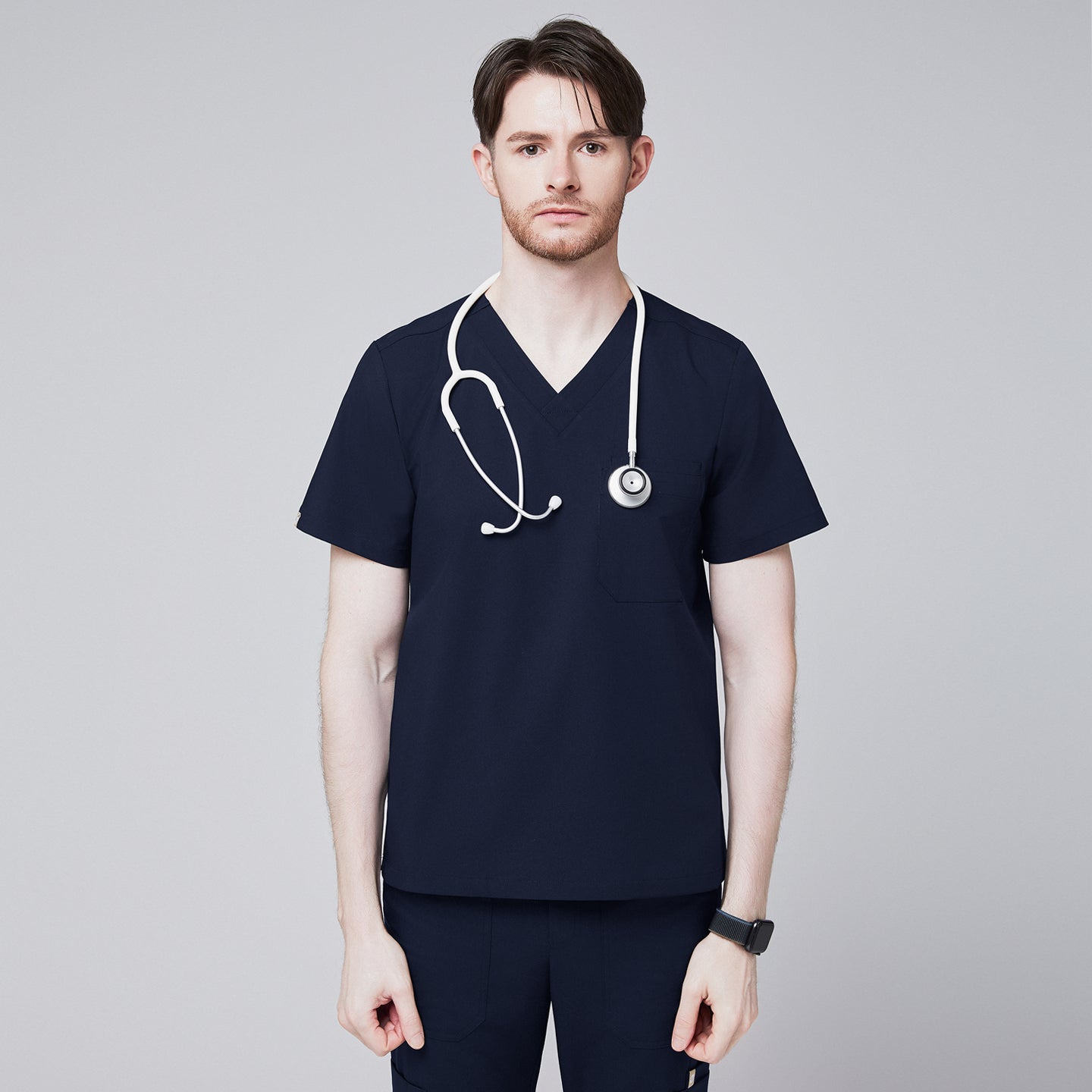 Male healthcare professional wearing a navy V-neck, three-pocket scrub top with stethoscope around neck, standing against a plain background,Navy