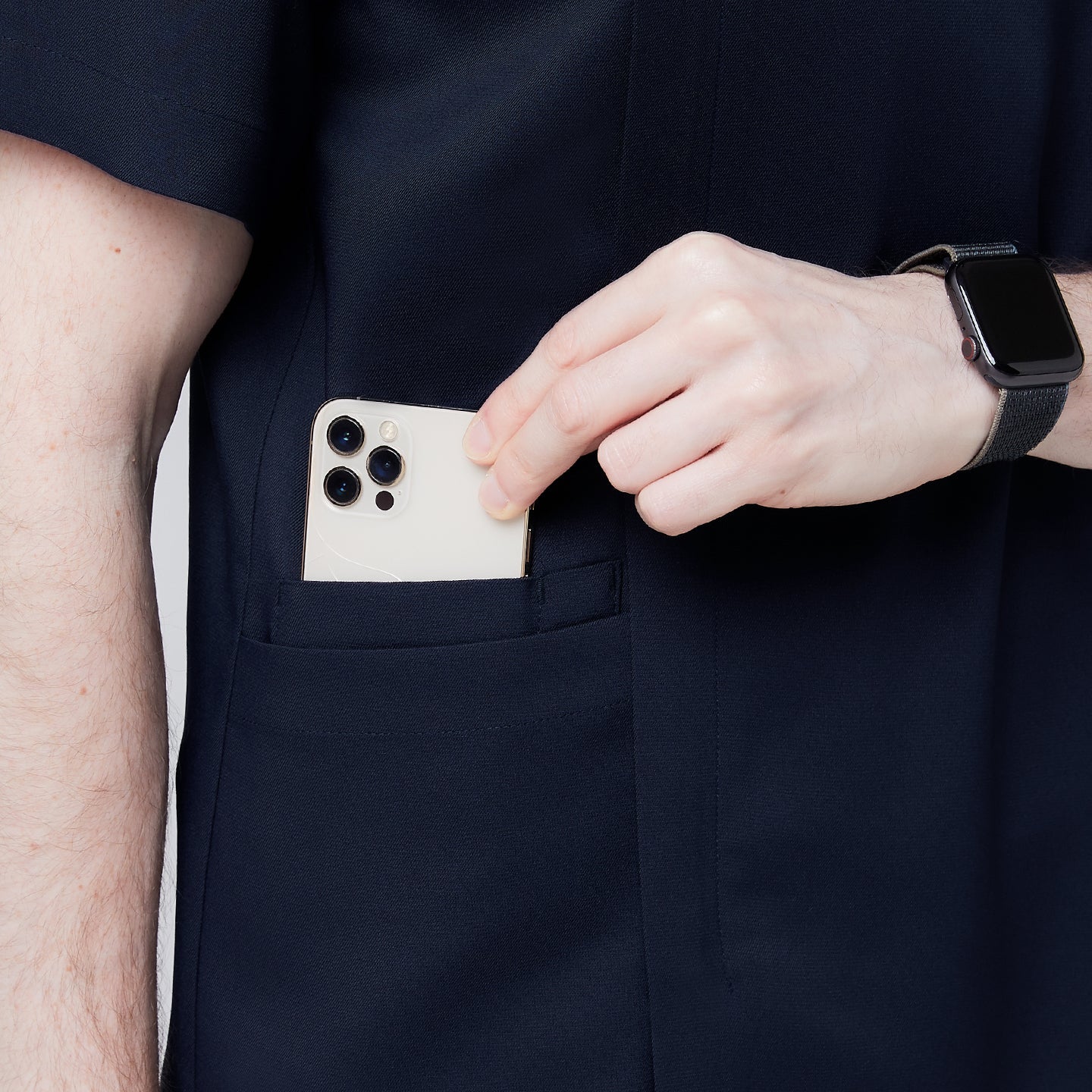 Close-up of a man's hand placing a smartphone into the pocket of a navy scrub top, showcasing the functionality and convenience of the pocket design,Navy