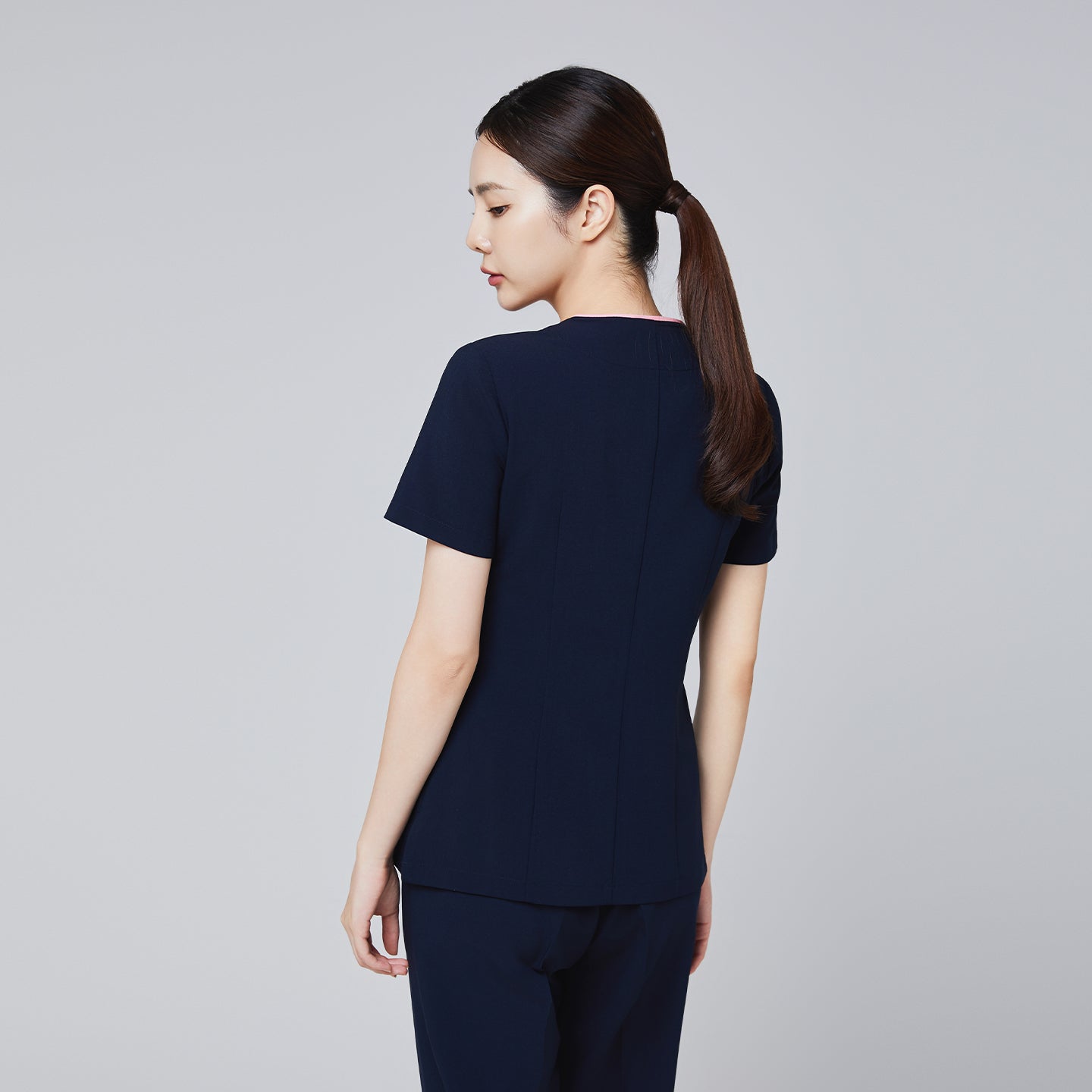 Back view of a navy scrub top with short sleeves and a streamlined, tailored fit, modeled by a woman,Navy