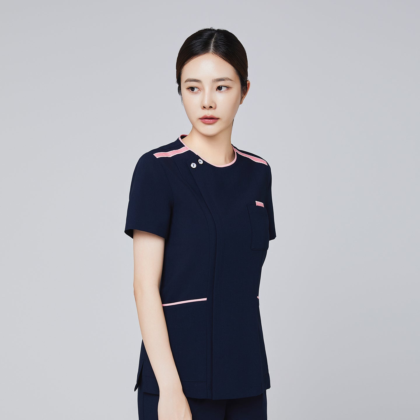 Navy scrub top with pink accents and a modern design, featuring a front pocket and short sleeves, modeled by a woman,Navy