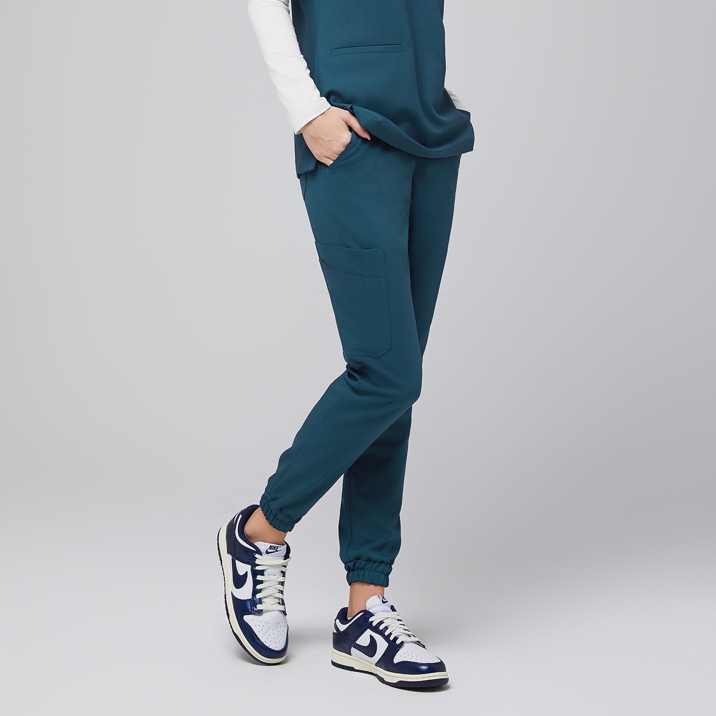 Female wearing teal jogger scrub pants with hands in pockets, side view, paired with navy and white sneakers,Ocean Teal