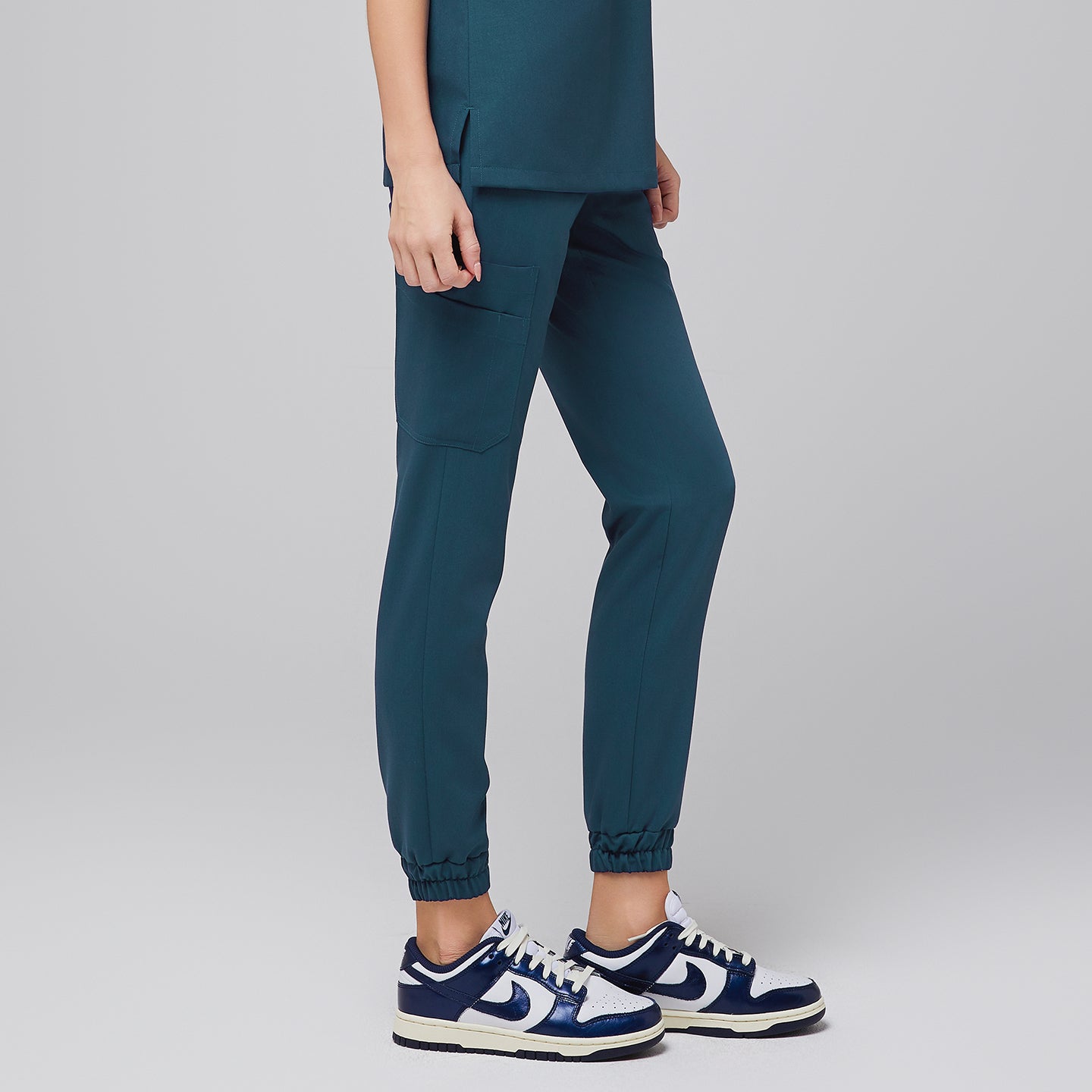 Female wearing teal jogger scrub pants with side pockets and elastic cuffs, shown from the side, paired with navy and white sneakers,Ocean Teal