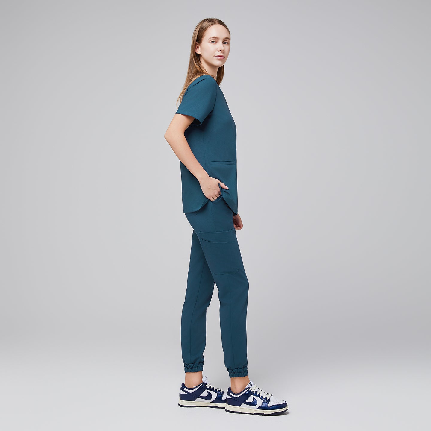 Female wearing teal jogger scrub pants and top, shown from the side with hands in pockets, paired with navy and white sneakers,Ocean Teal