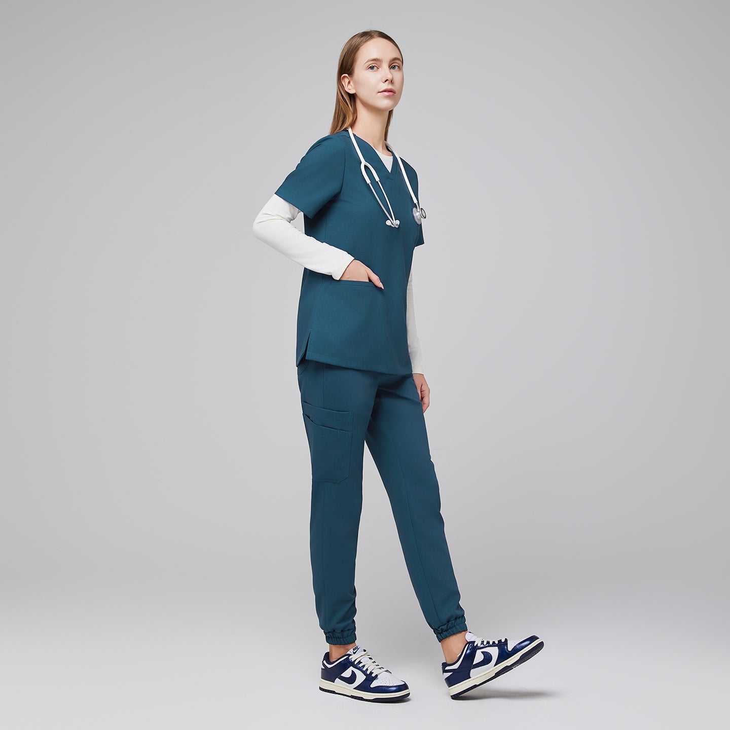 Female wearing teal jogger scrub pants and top with a stethoscope, standing with hands in pocket, paired with navy and white sneakers,Ocean Teal