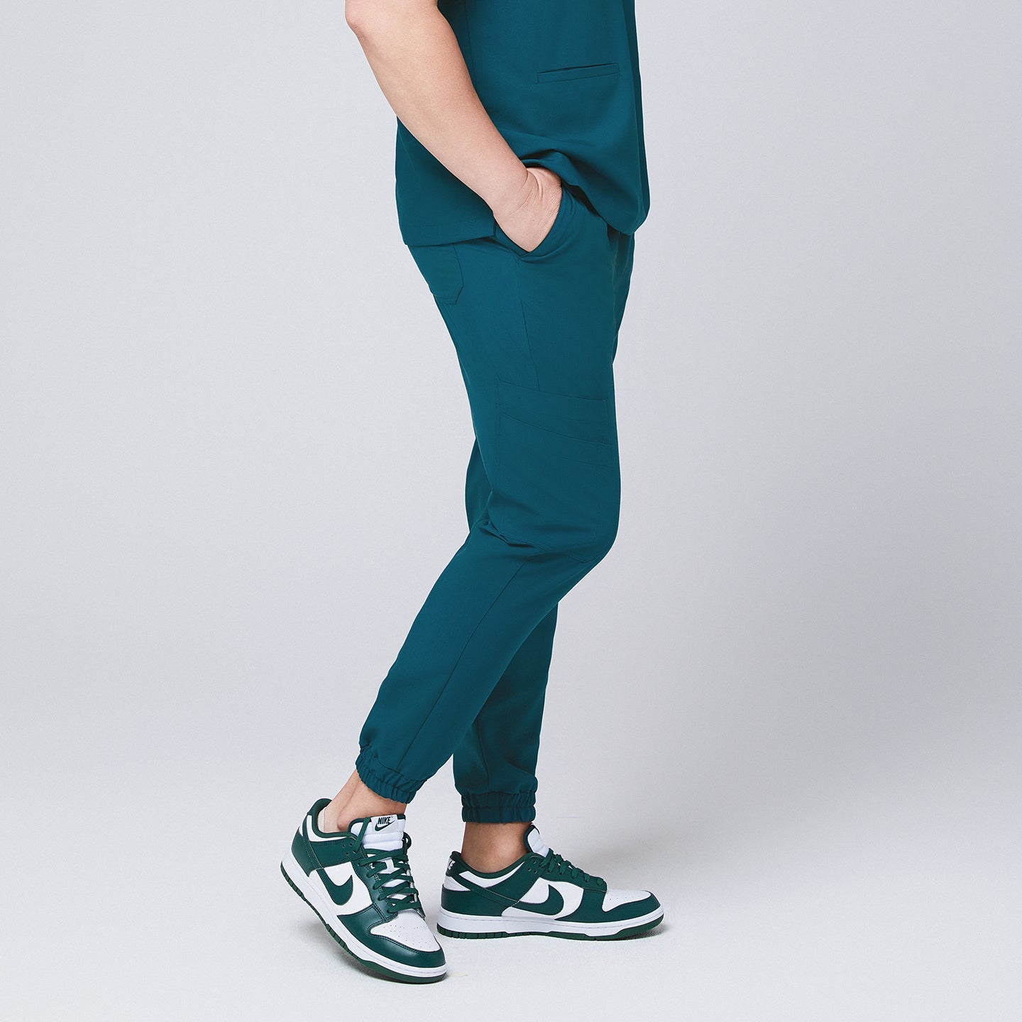 Ocean teal jogger scrub pants made of stretchy fabric and matching ocean teal scrub top, with teal sneakers and hands in pocket,Ocean teal