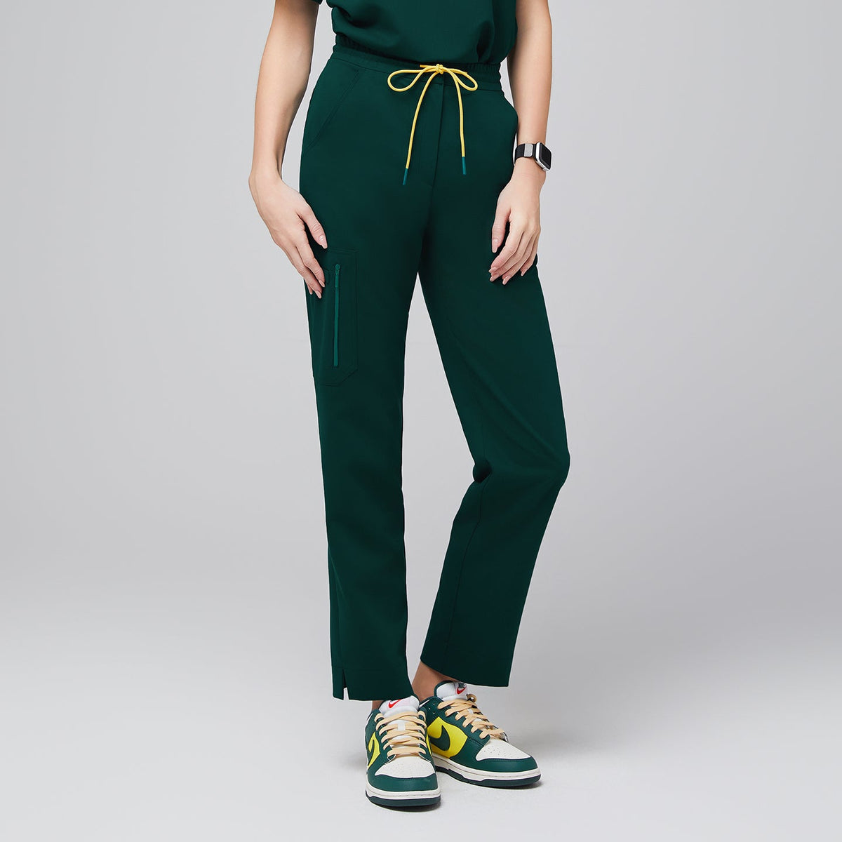 Scrub pants with a drawstring waist, zipper pocket, and split hem, paired with sporty sneakers for a functional and professional style,Pine Green