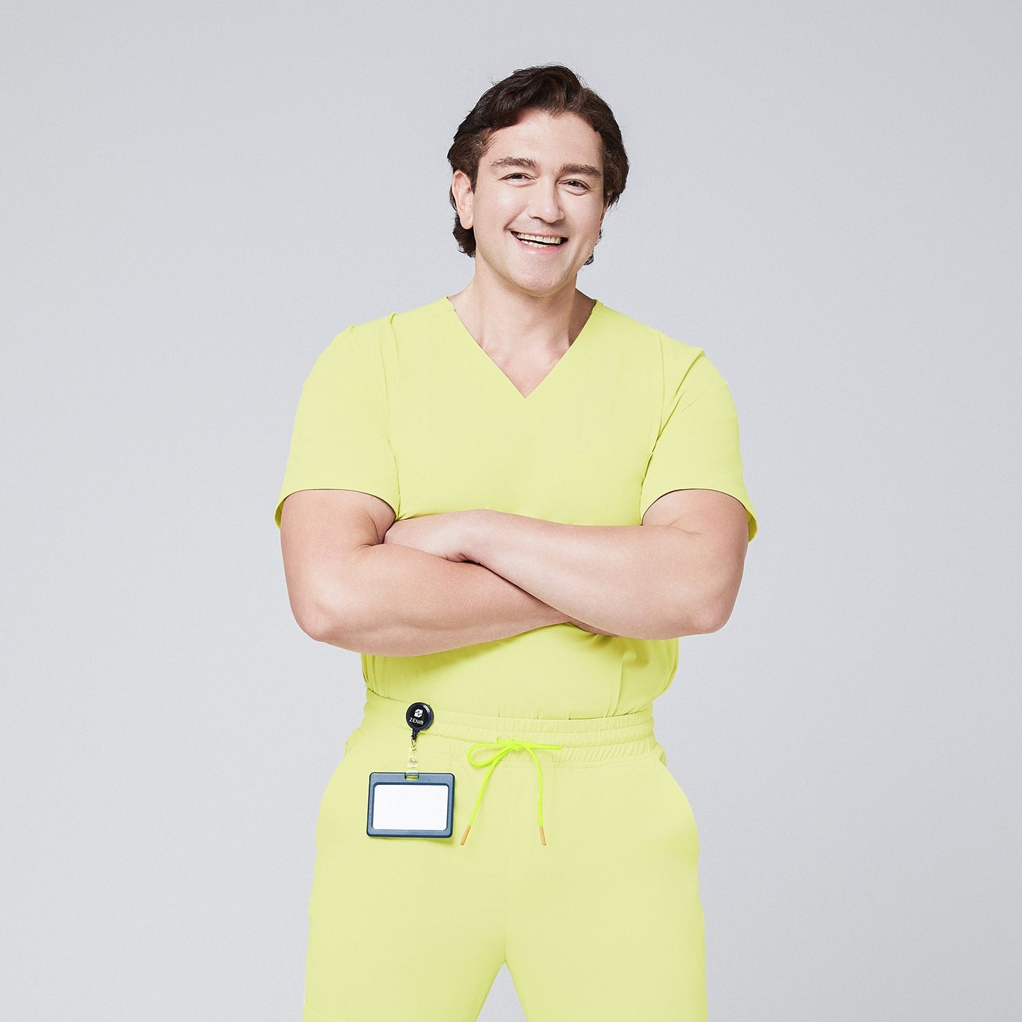 Male model wearing a pineapple yellow V-neck single-pocket scrub top with matching pants and a badge holder, smiling with arms crossed,Pineapple Yellow