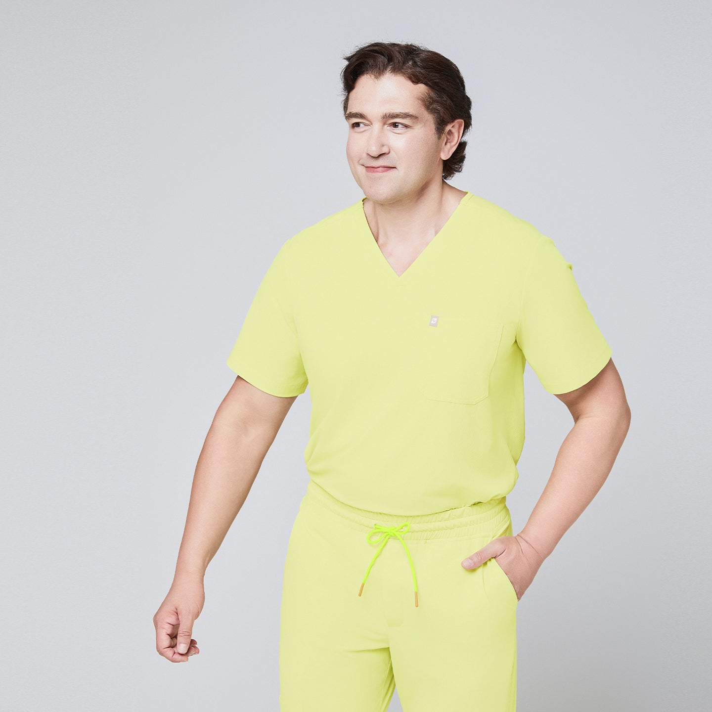 Male model wearing a pineapple yellow V-neck single-pocket scrub top with matching drawstring pants, smiling,Pineapple Yellow