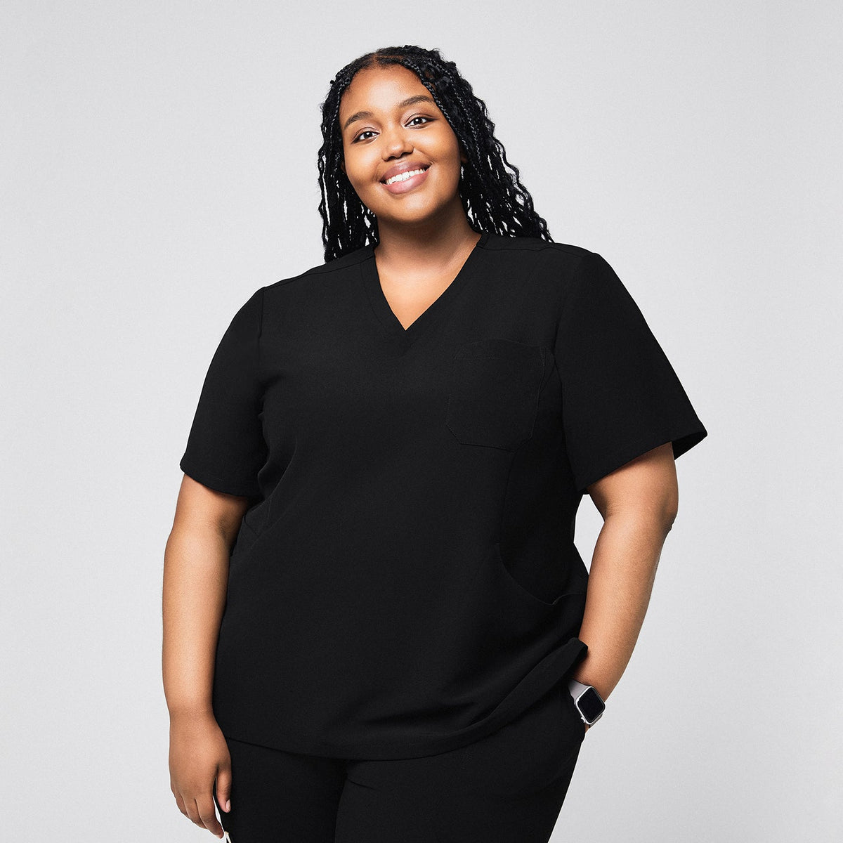 Smiling female medical professional wearing a black scrub top with a single chest pocket, standing with her hand in her pocket,Rich Black