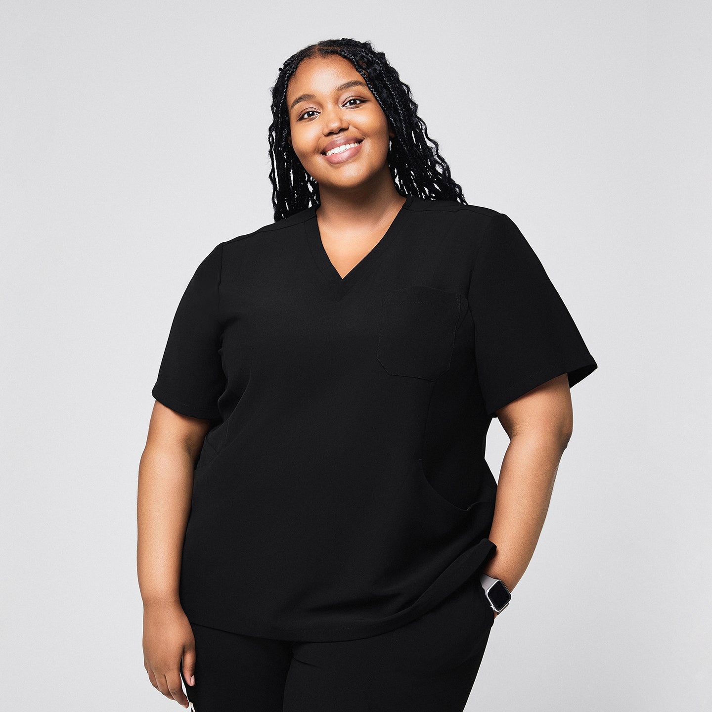 Smiling female medical professional wearing a black scrub top with a single chest pocket, standing with her hand in her pocket,Rich Black