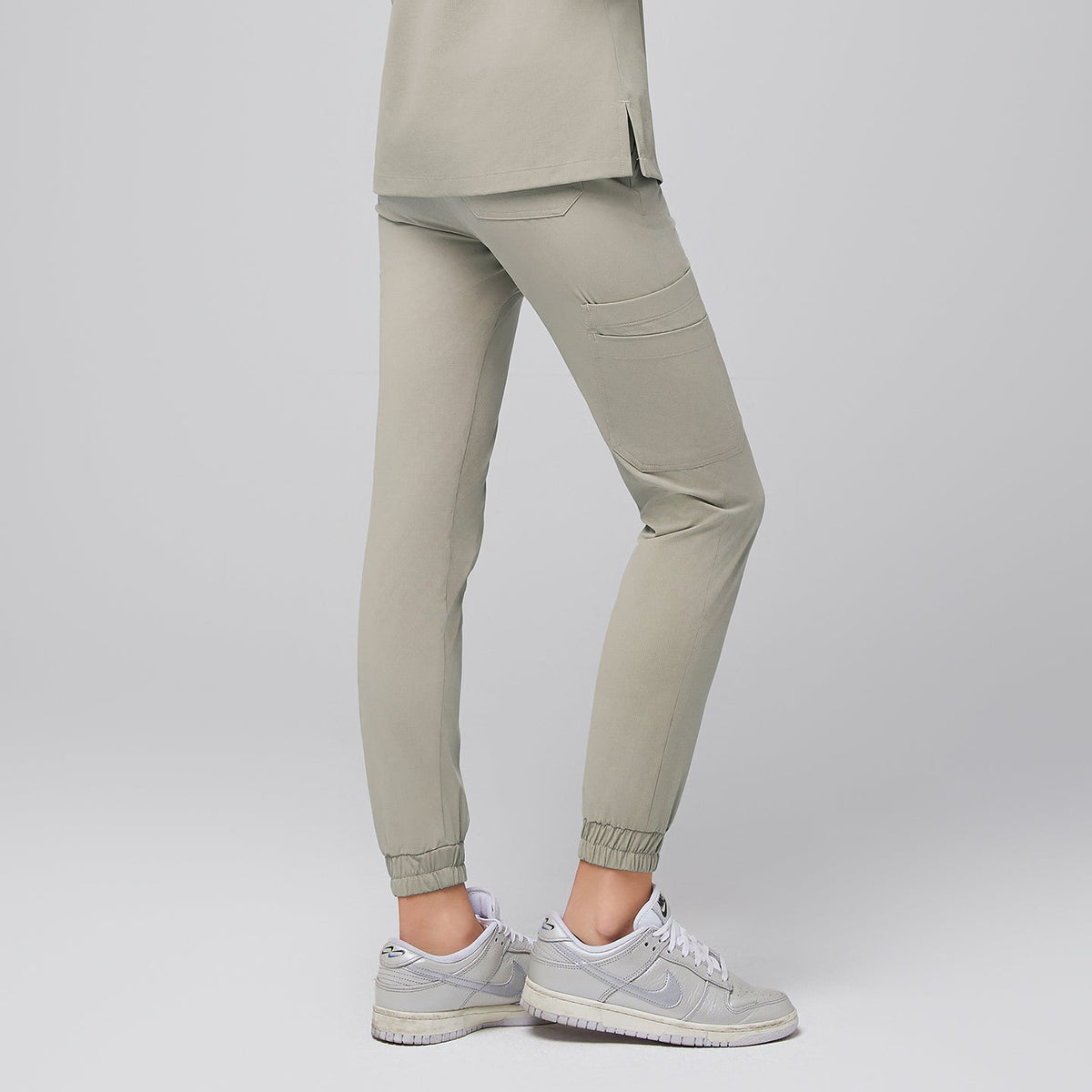 Back view of sand khaki jogger scrub pants showcasing a tailored fit with back pockets and elasticized cuffs, paired with sleek silver sneakers for a modern and professional appearance, Sand Khaki