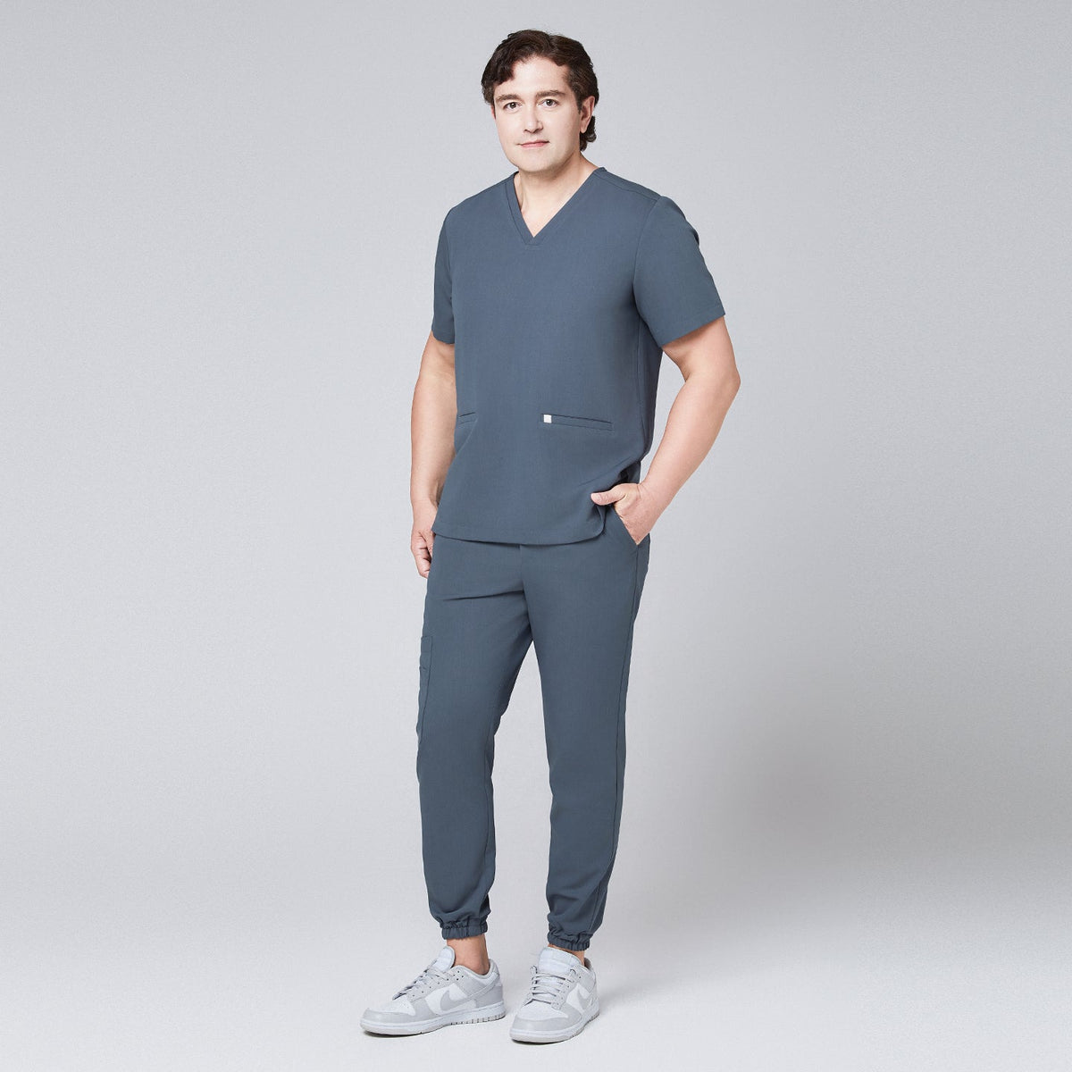 Full-body view of a man in a smoky blue scrub set with jogger pants and a double-pocket V-neck top,Smoky Blue