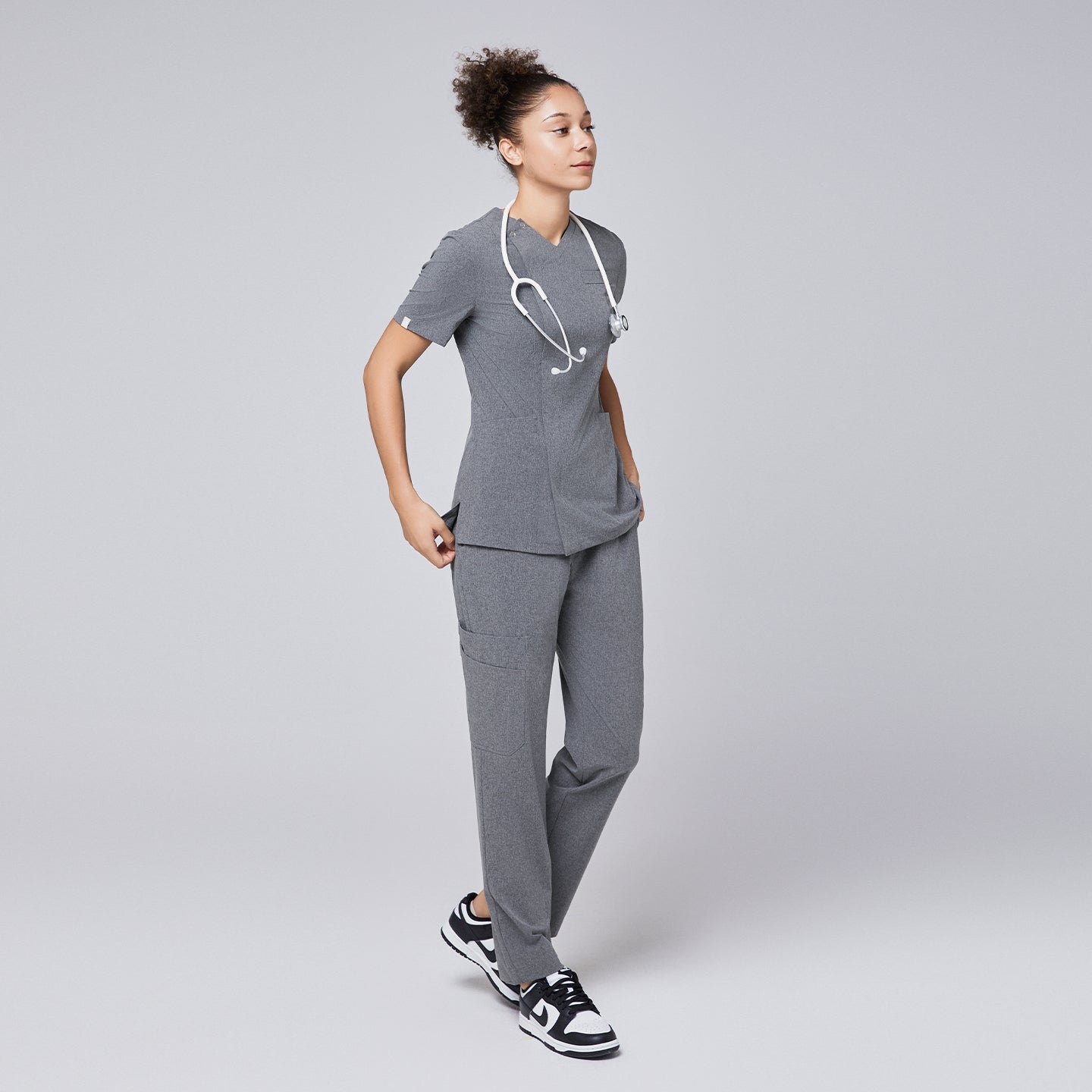 Woman wearing Zenir soft gray front zipper scrub set with a stethoscope and black and white sneakers,Ash Gray