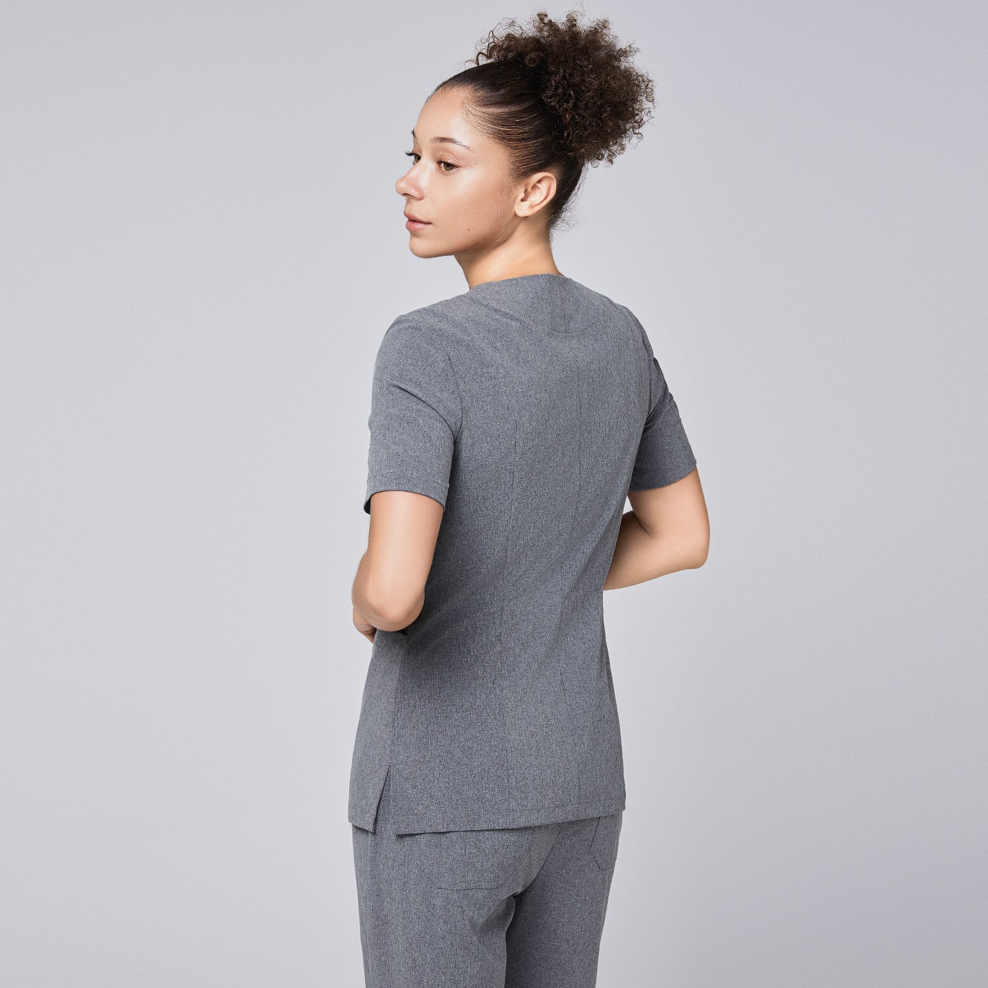 Woman wearing Zenir soft gray front zipper scrub top, showing the back view, paired with matching pants,Ash Gray