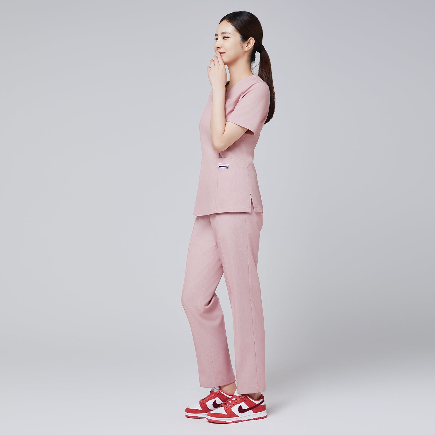 Side view of soft pink scrub set with a V-neck top and straight-leg pants, styled with red Nike sneakers,Soft Pink