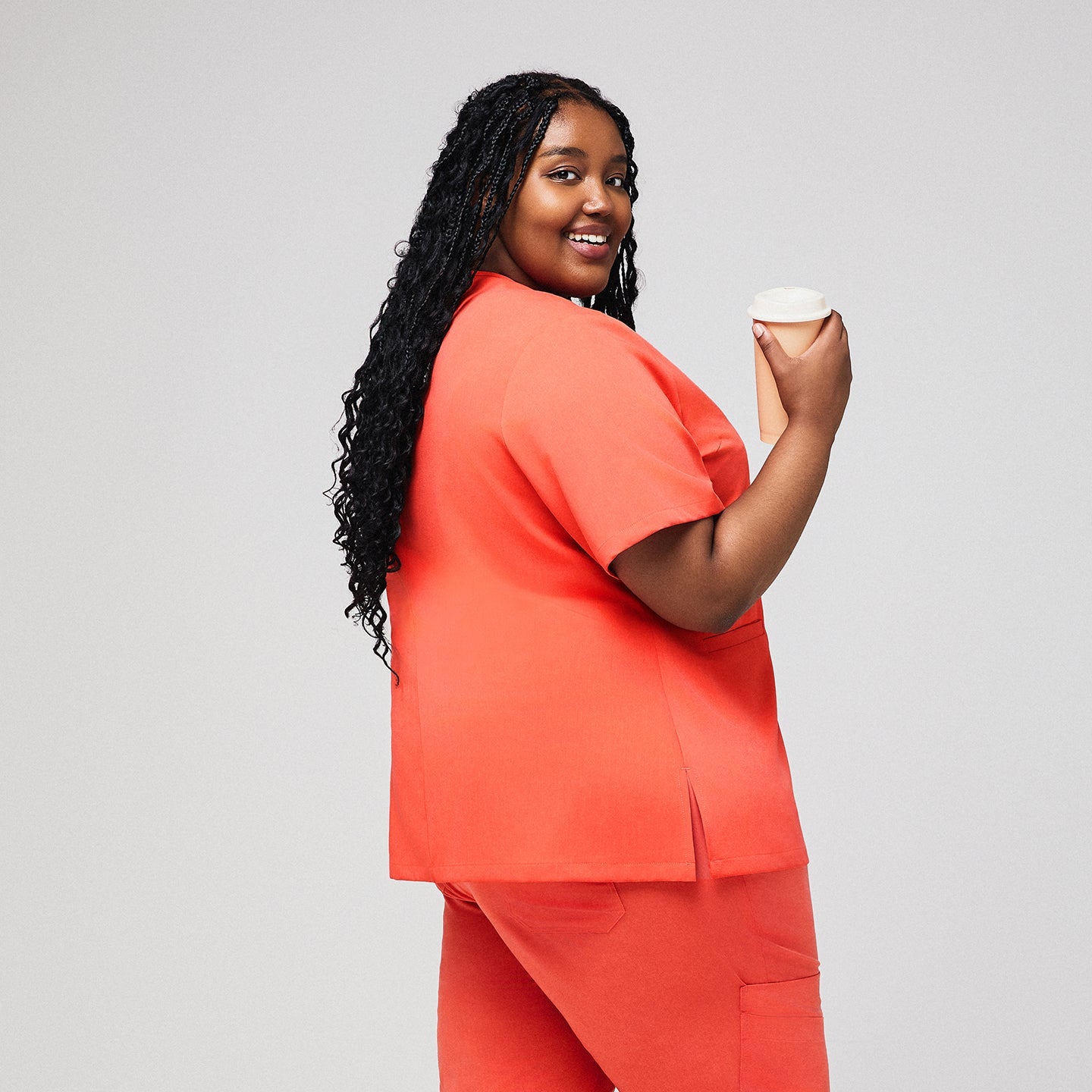 Plus-size healthcare professional in Tiger orange scrub set holding a coffee cup, viewed from the back,Tiger Orange