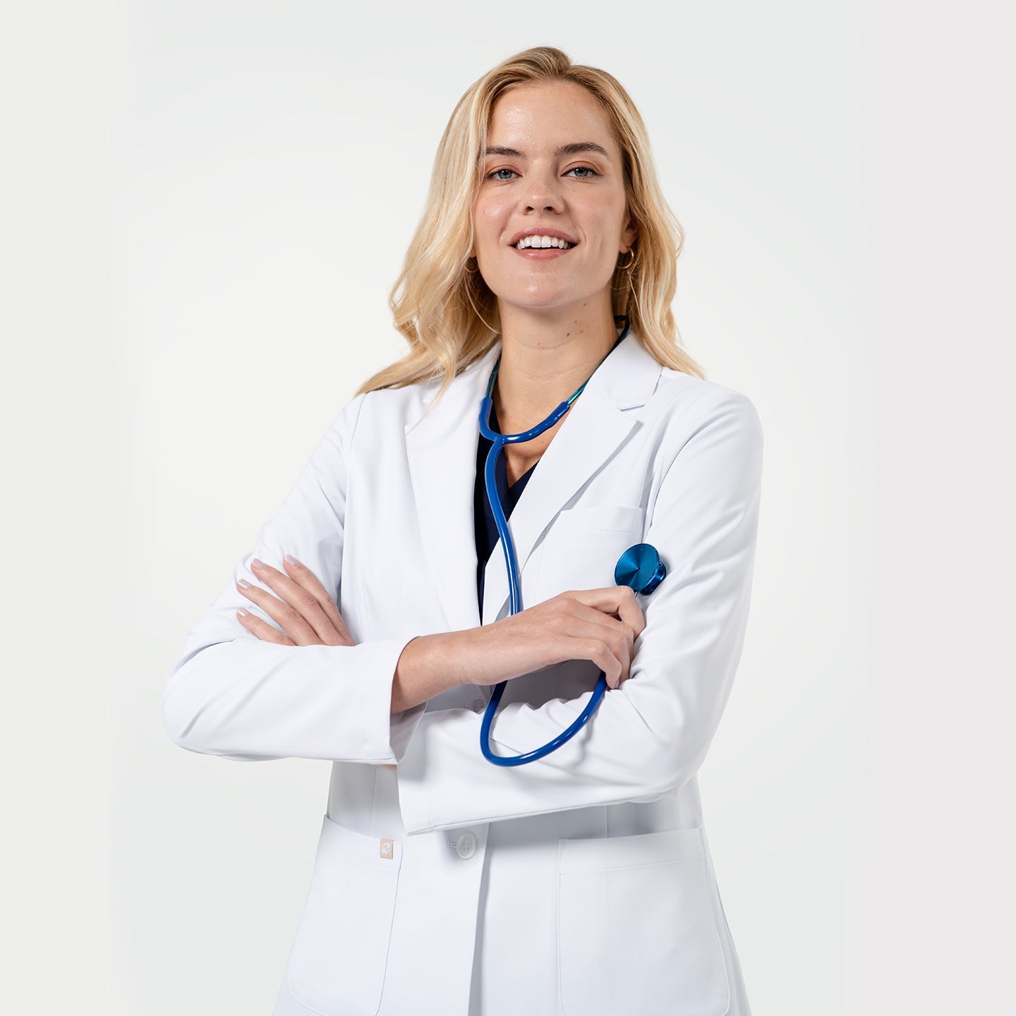 A smiling doctor wearing a white lab coat and stethoscope, standing on a light gray background in a professional mood.