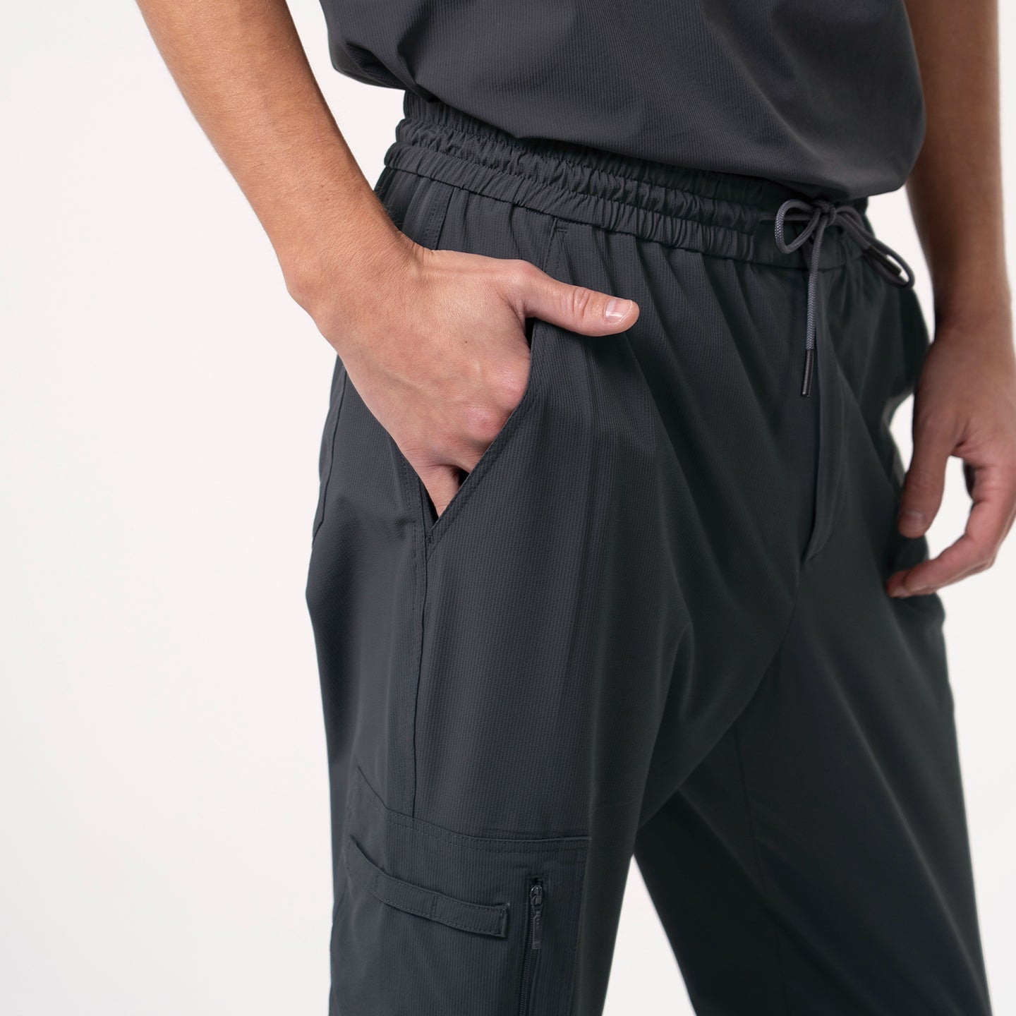 Close-up of Deep Gray Zipper Pocket Jogger Scrub Pants, showing the left hand placed in the side pocket with an elastic waistband and visible pocket detail.