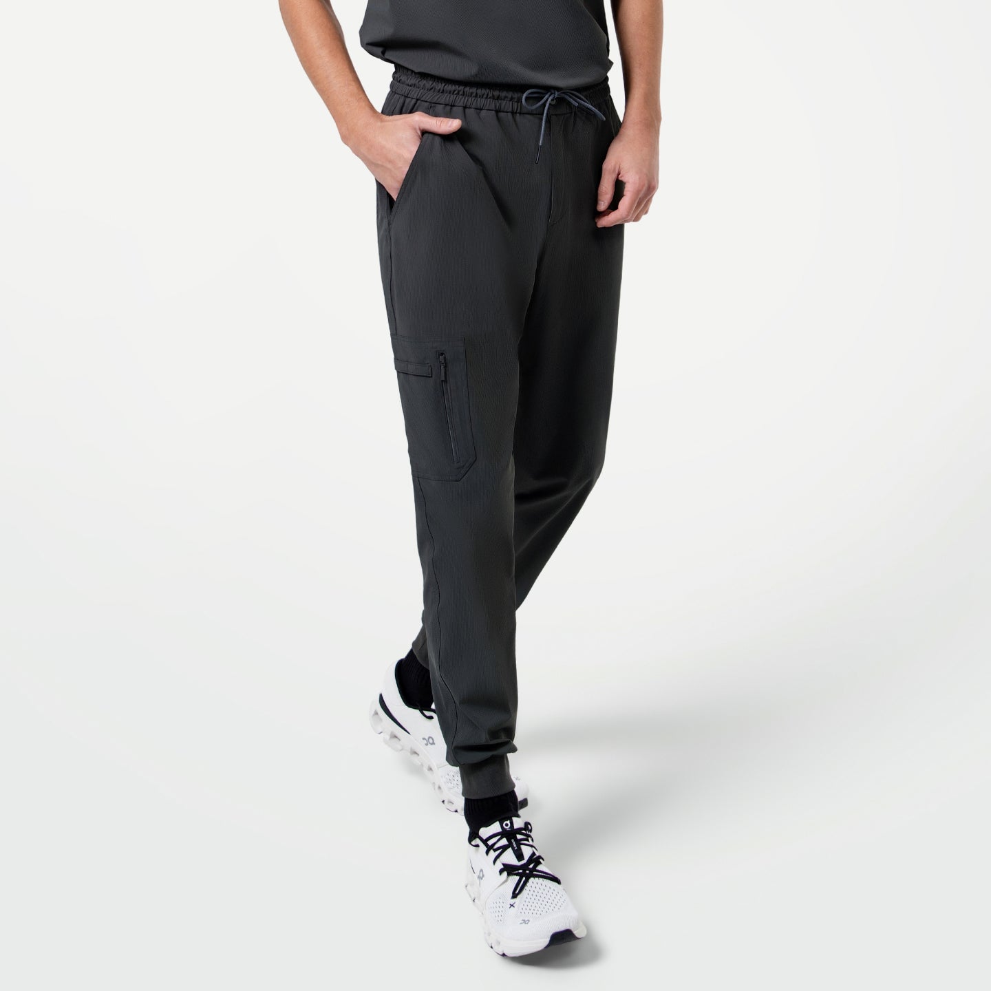 Male model in mid-step with one hand in his pocket, showcasing Zipper Pocket Jogger Scrub Pants in Deep Gray paired with a matching scrub top and white sneakers.