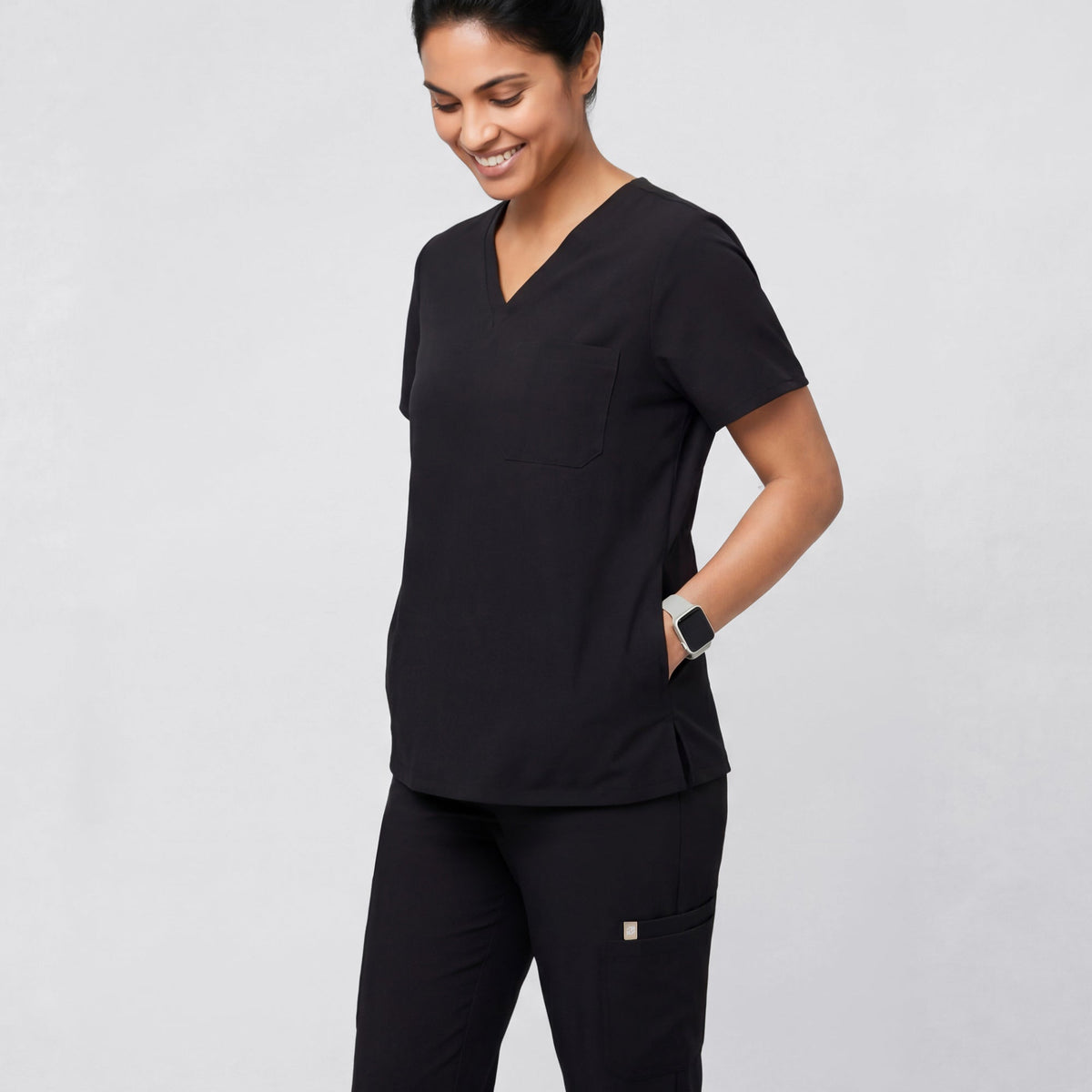Model wearing the Eco Black 3-Pocket Scrub Top in a relaxed side pose, showing the V-neckline and chest pocket.